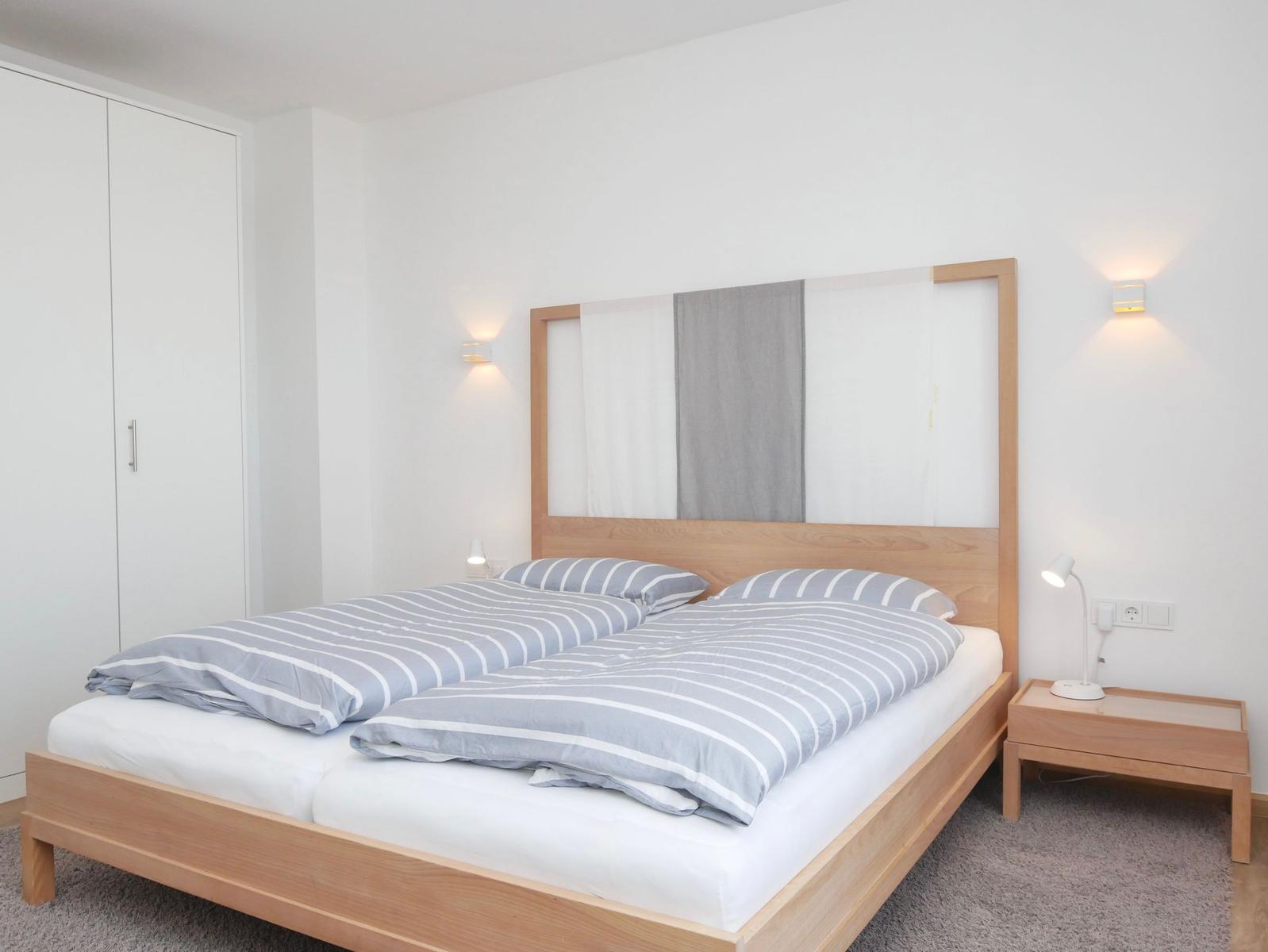 Schlafzimmer mit Doppelbett, Holzbettgestell, Nachttisch und Kleiderschrank.