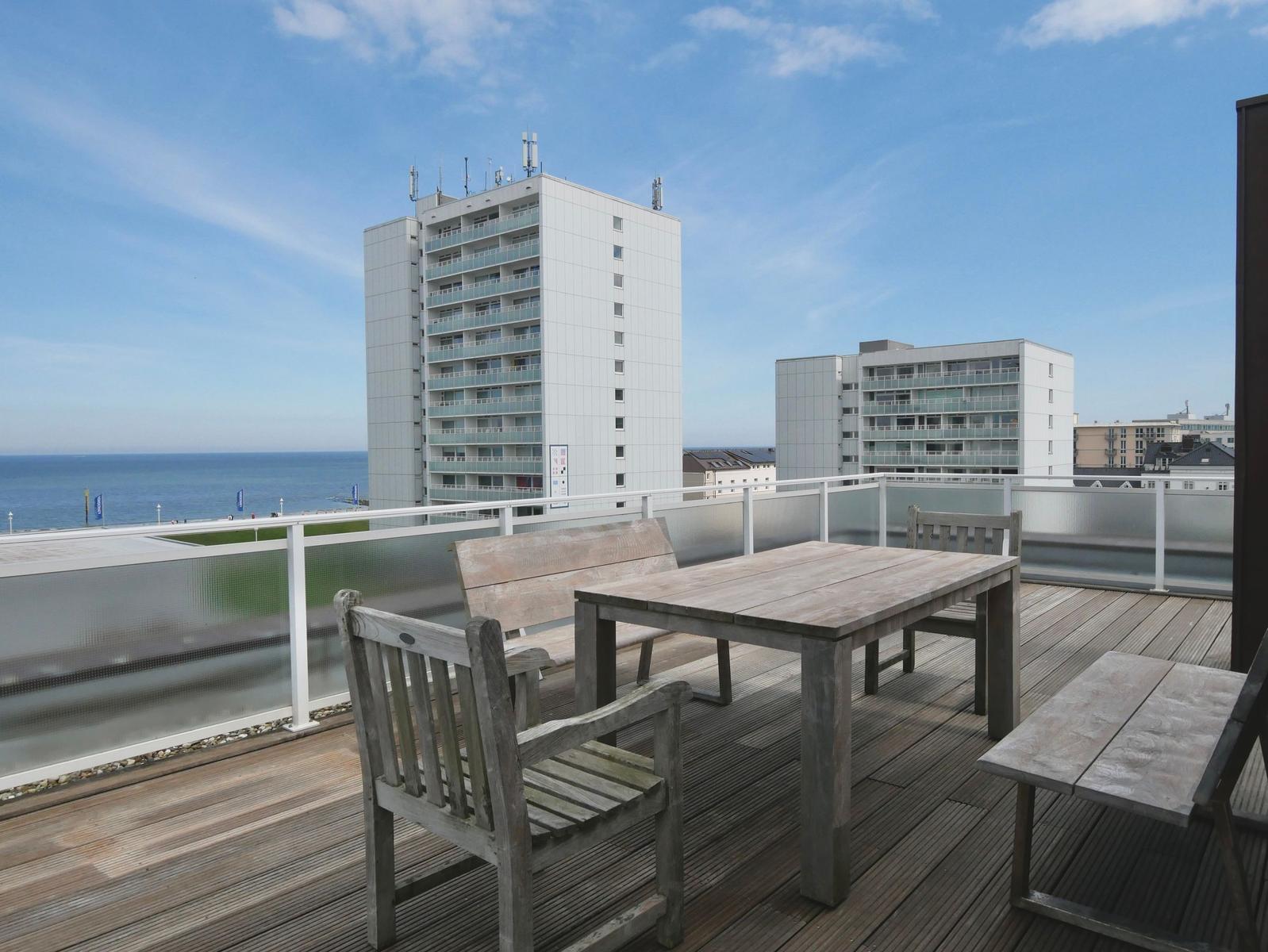 Terrasse mit Tisch und Bänken. Blick auf Meer und Hochhäuser.