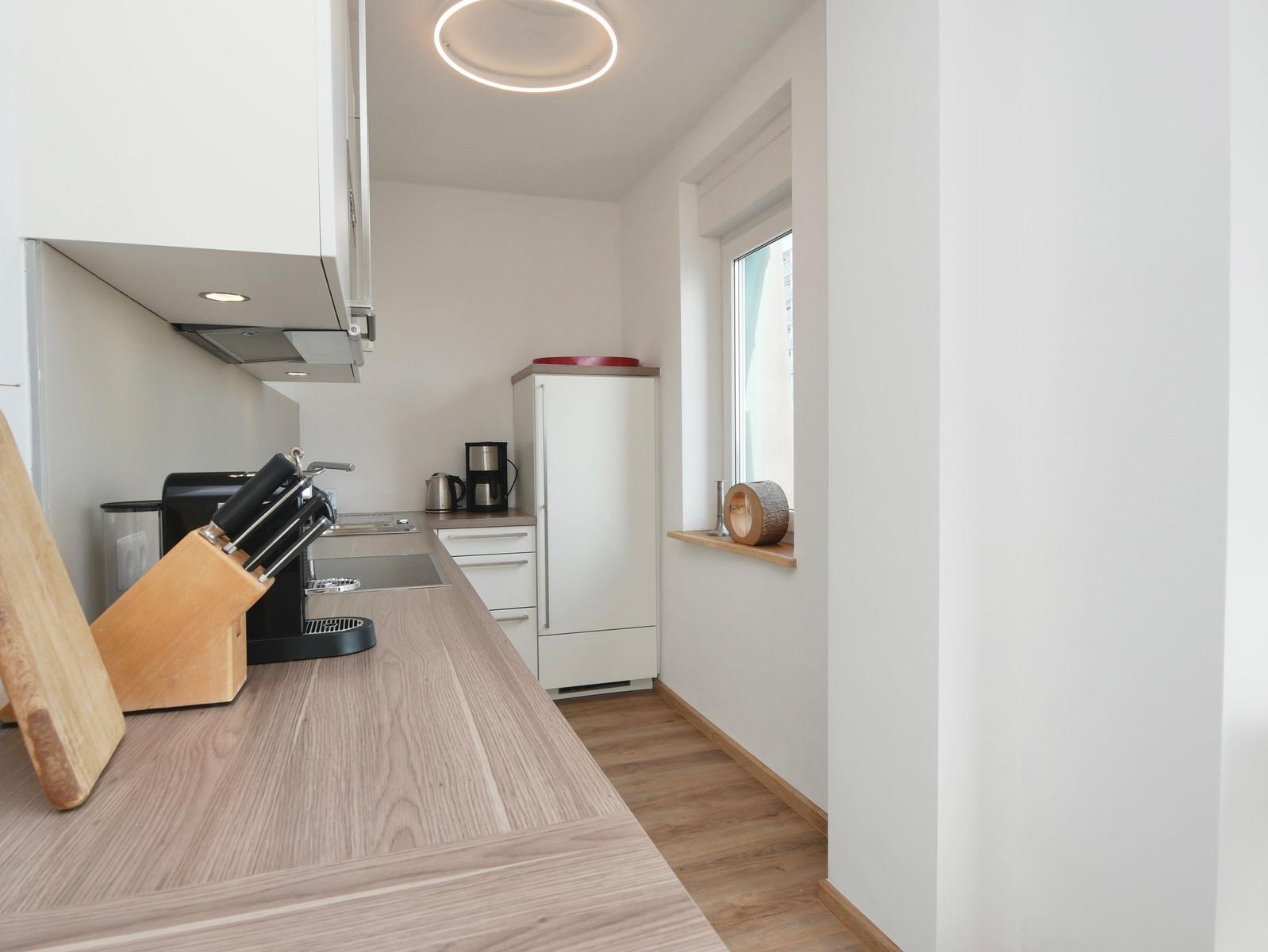 Küche mit Arbeitsplatte, Kühlschrank und Fenster