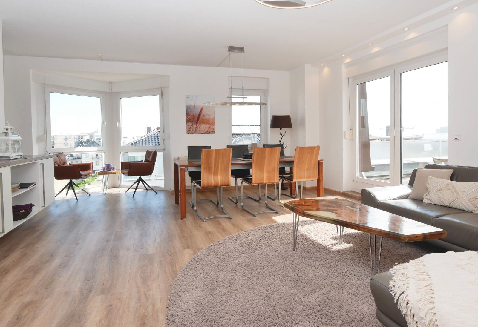 Wohn- und Essbereich mit Holzboden, Sofa, Esstisch und Blick auf Balkon.