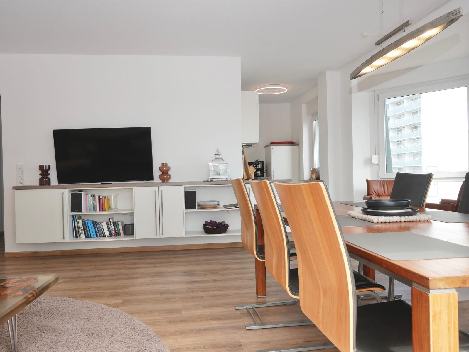 Wohn- und Essbereich mit TV, Bücherregal und Holztisch mit Stühlen.
