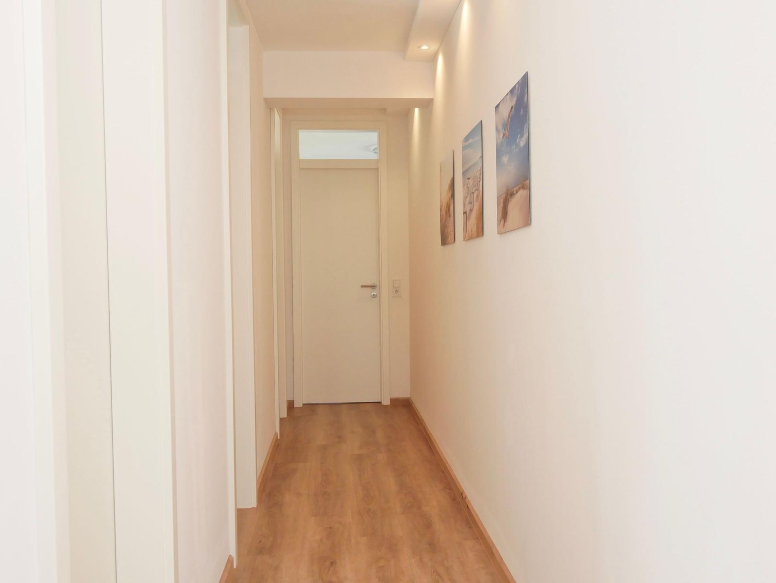 Flur mit Holzboden, weißen Wänden und drei Wandbildern an der rechten Wand.