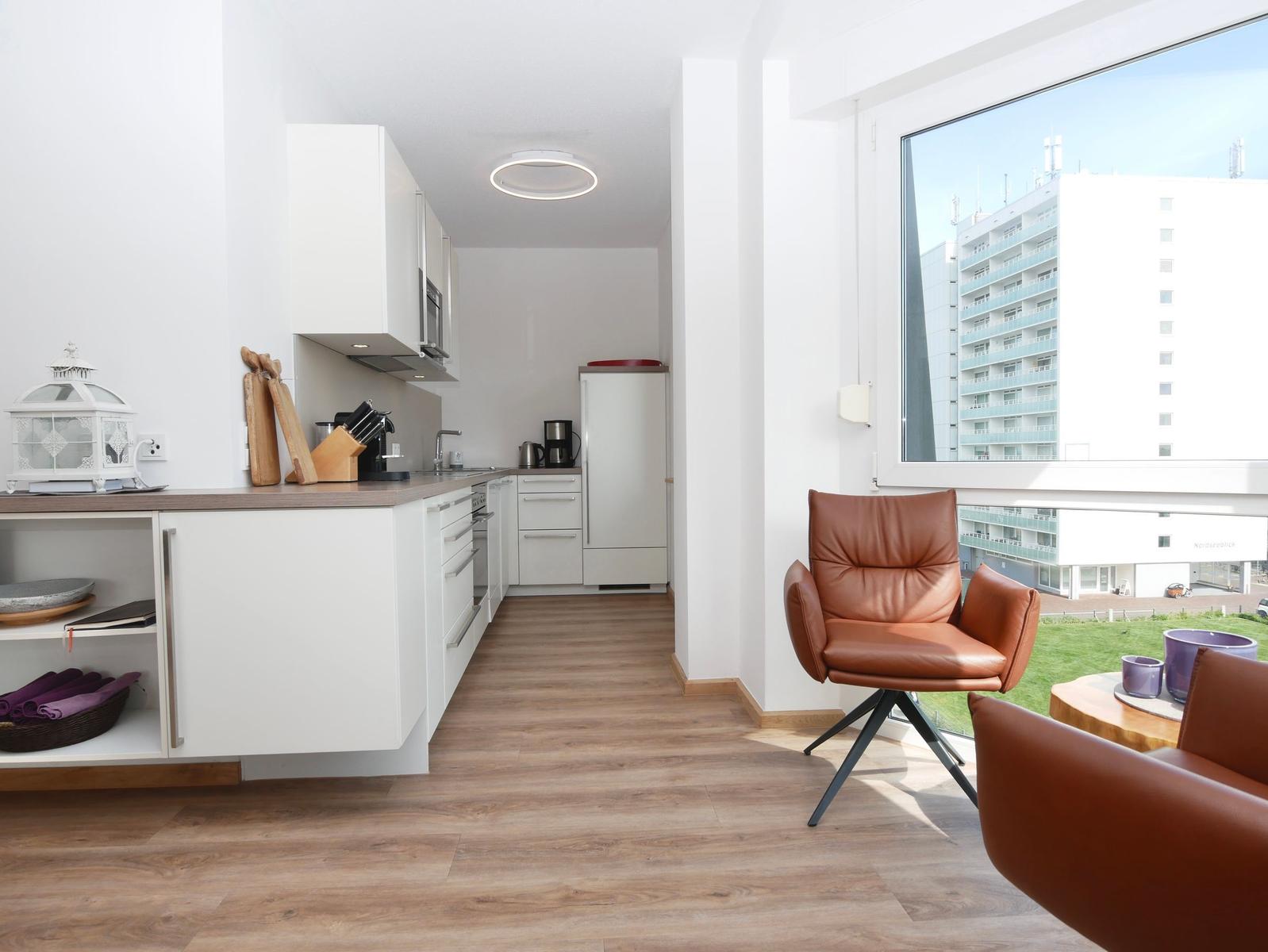 Küche mit Arbeitsfläche, Kühlschrank und Sitzgelegenheit mit braunem Stuhl.