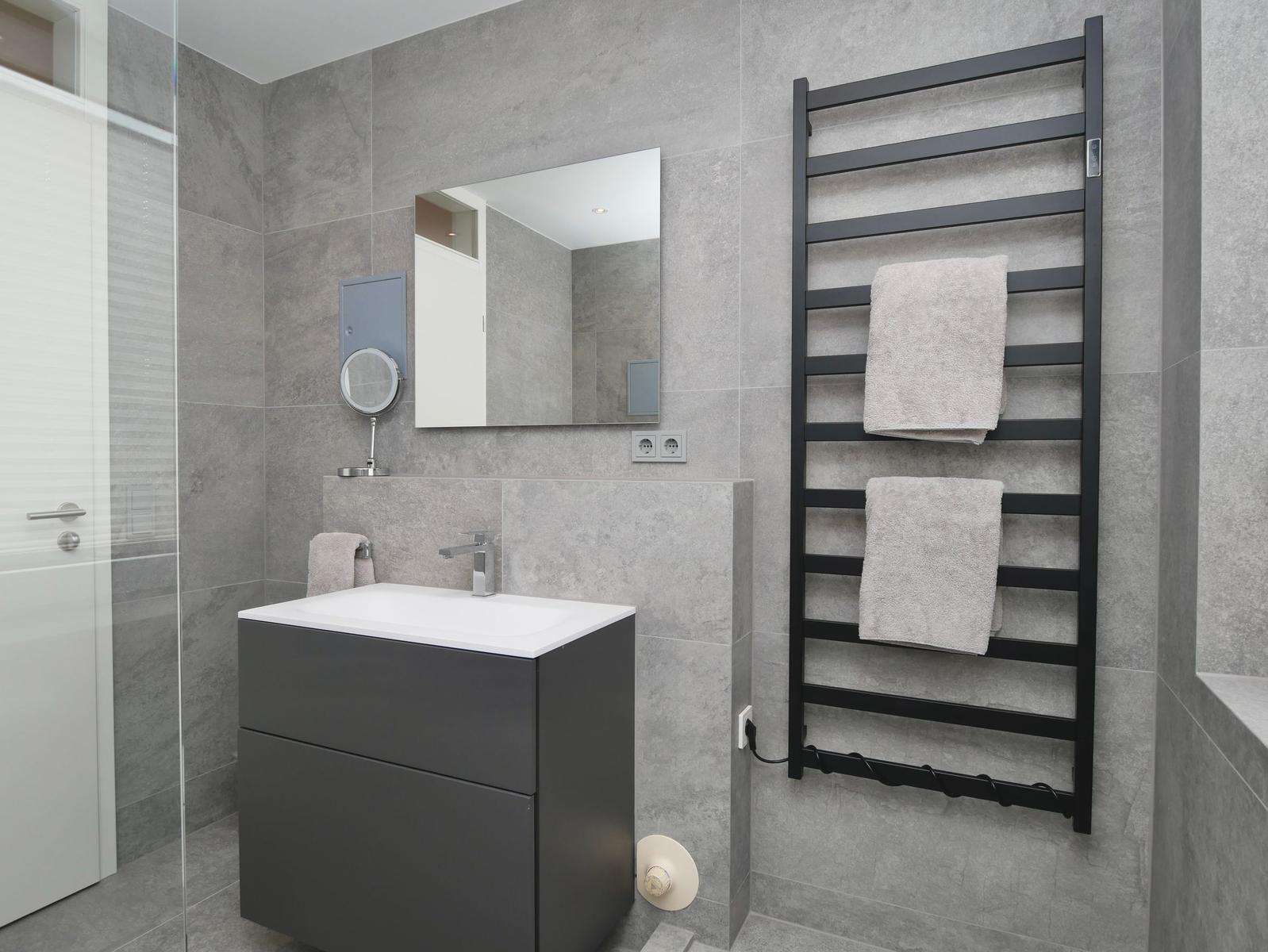 Badezimmer mit Waschbecken, Spiegel und Handtuchheizung an der Wand.
