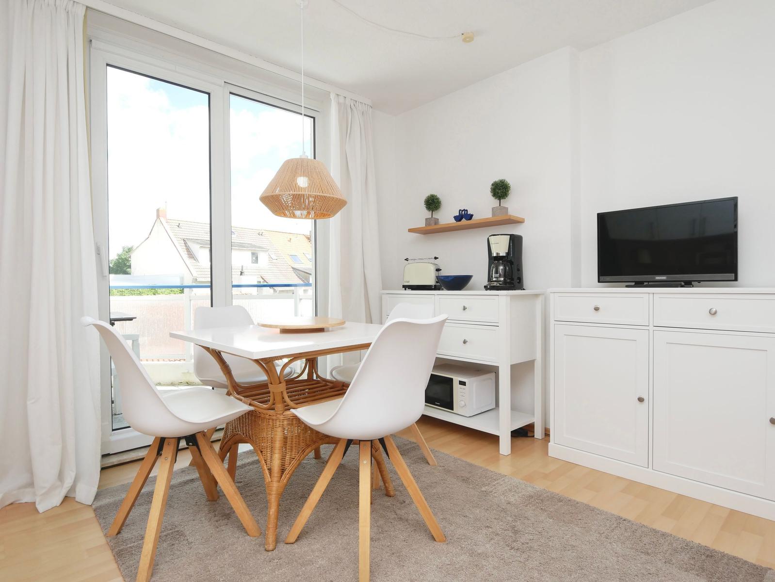 Essbereich mit Tisch, Stühlen und TV. Durchgangstür zum Balkon.