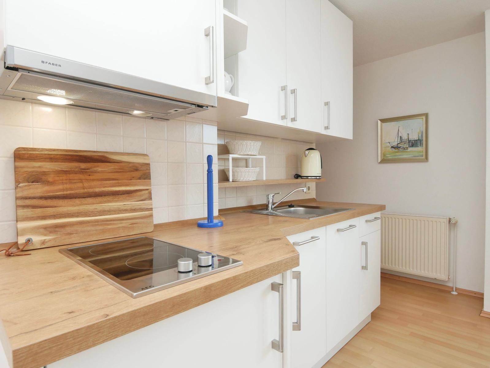 Küche mit Holzplatte, Herd und Spüle. Weiße Schränke und Kachelwand.
