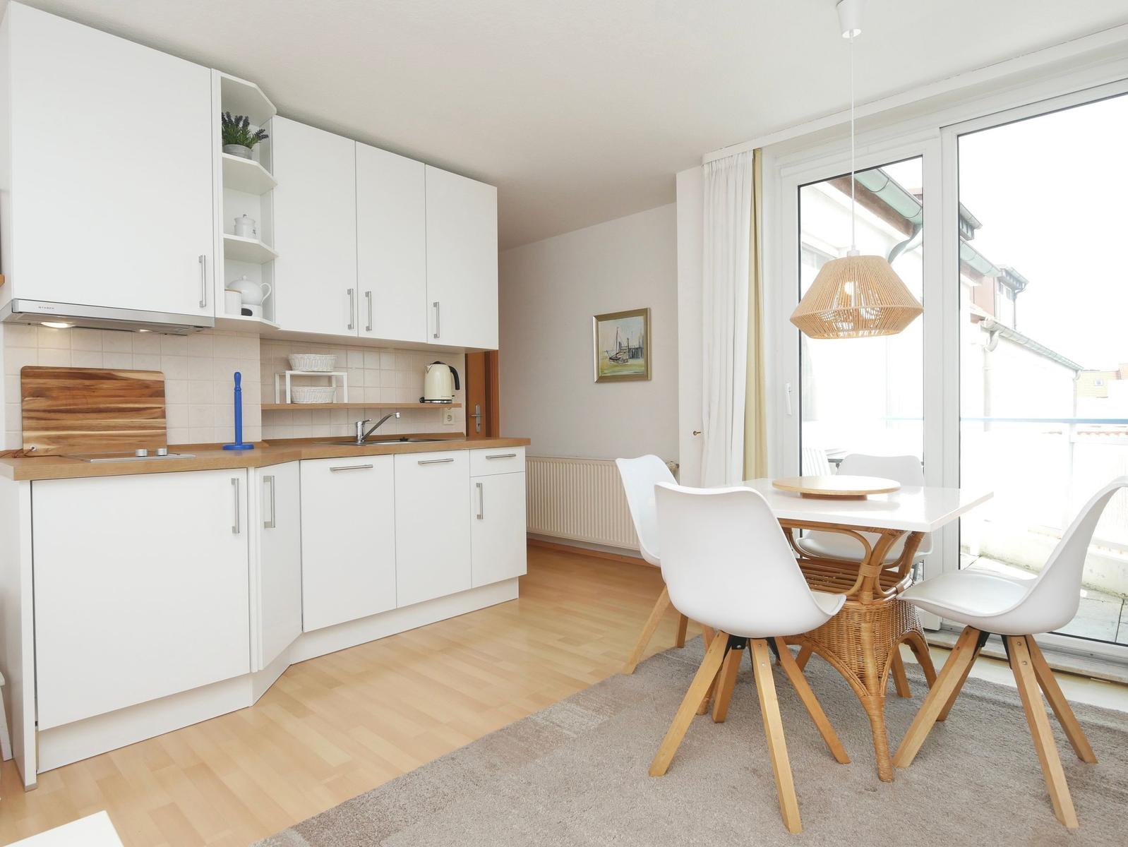 Küche mit Essbereich, weißer Tisch und Stühle, große Fensterfront mit Blick auf Balkon.
