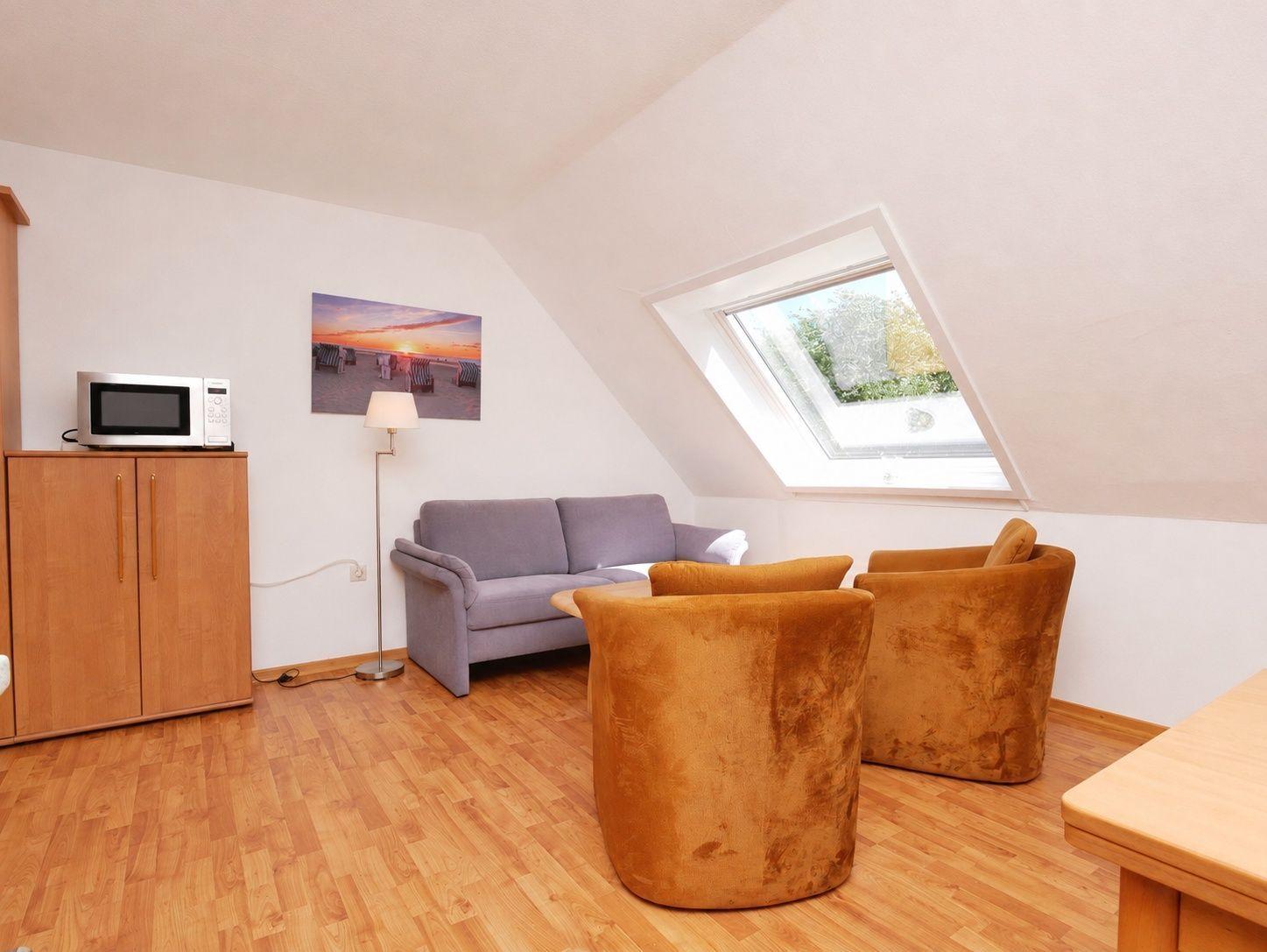 Wohnraum mit Sofa, zwei Sesseln, Mikrowelle und Dachfenster.