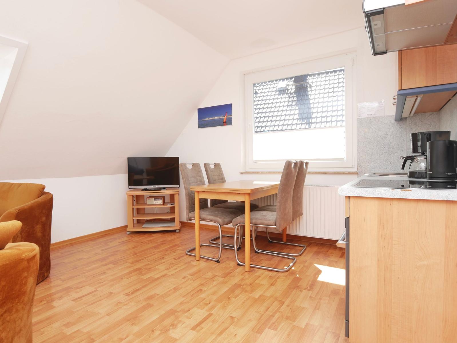 Wohnküche mit Essbereich, Fernseher und Fenster. Holzfußboden und Küchenzeile.