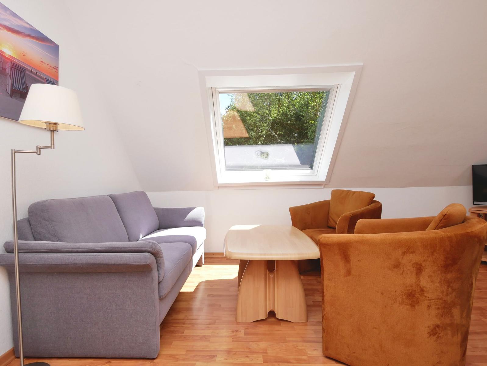 Wohnzimmer mit Sofa, zwei Sesseln, Tisch und Dachfenster.