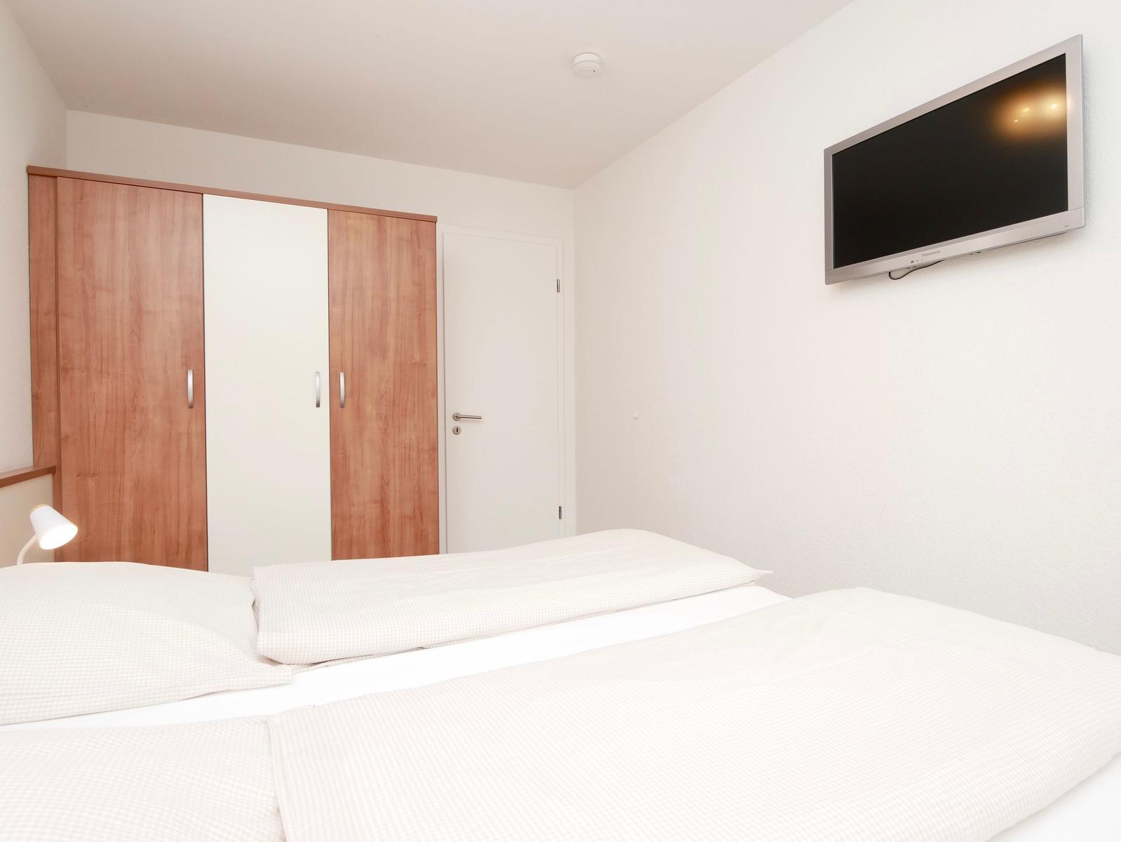 Schlafzimmer mit Bett, Kleiderschrank und Wandfernseher.