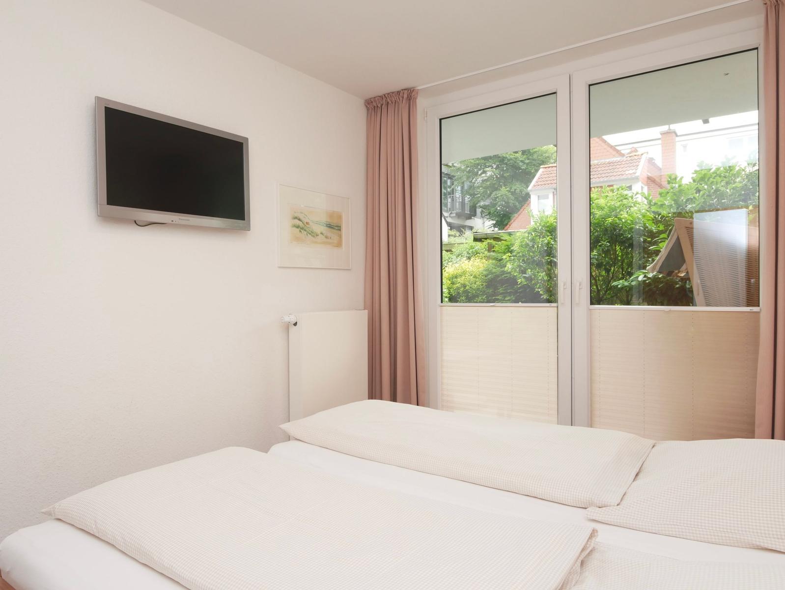 Schlafzimmer mit Doppelbett, Fernseher und Fenster mit Blick auf Grünflächen.