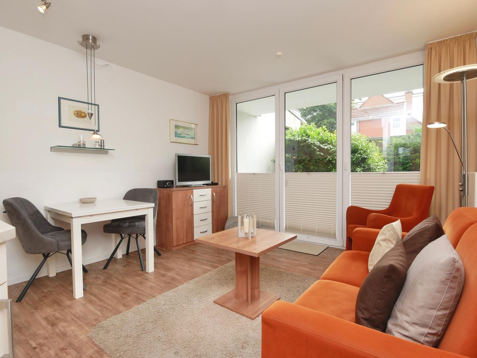 Wohnzimmer mit orangefarbenem Sofa, Essbereich und Glasfront zur Terrasse.