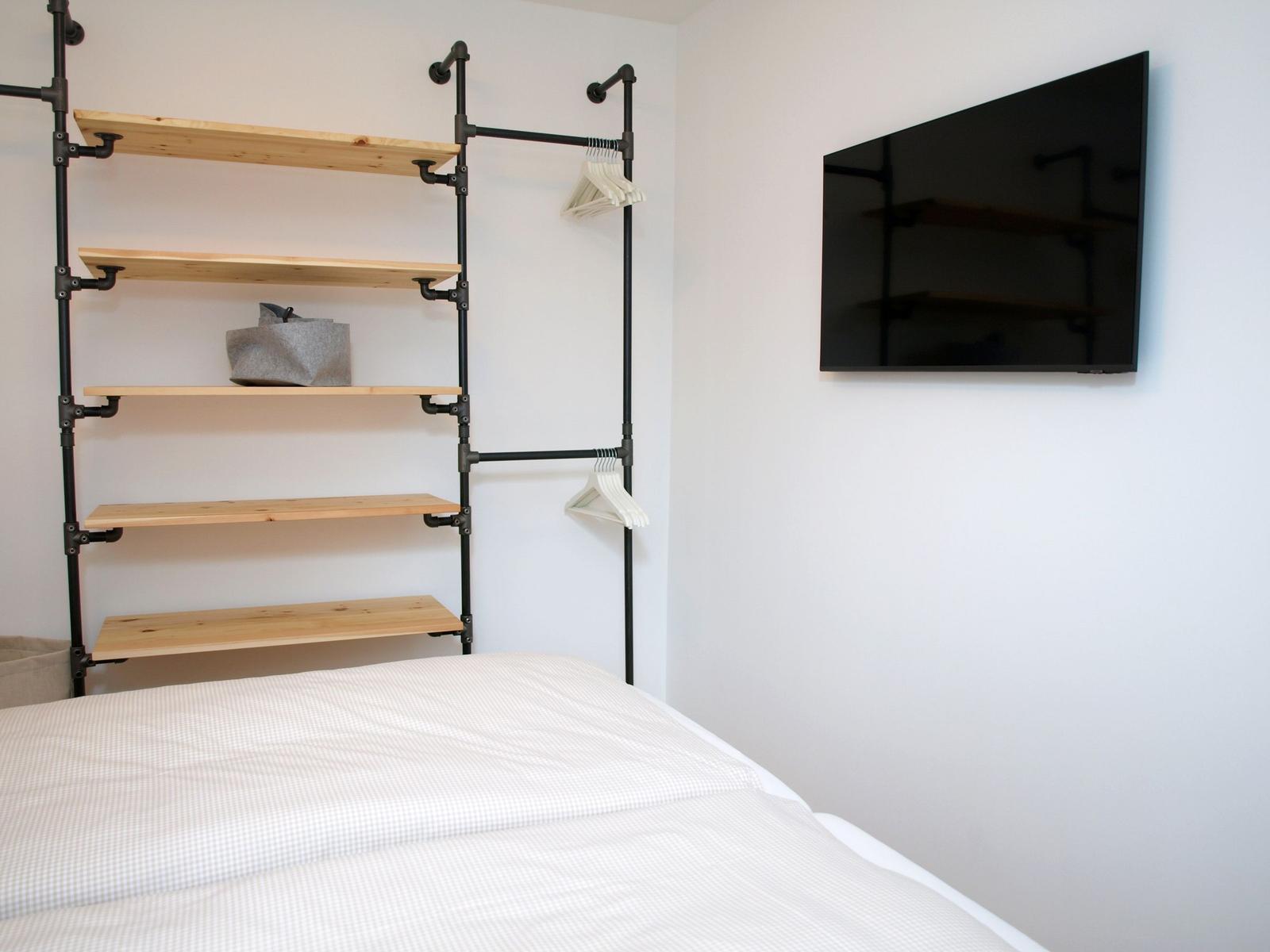 Schlafzimmer mit Bett, Wandregal und Flachbildfernseher.