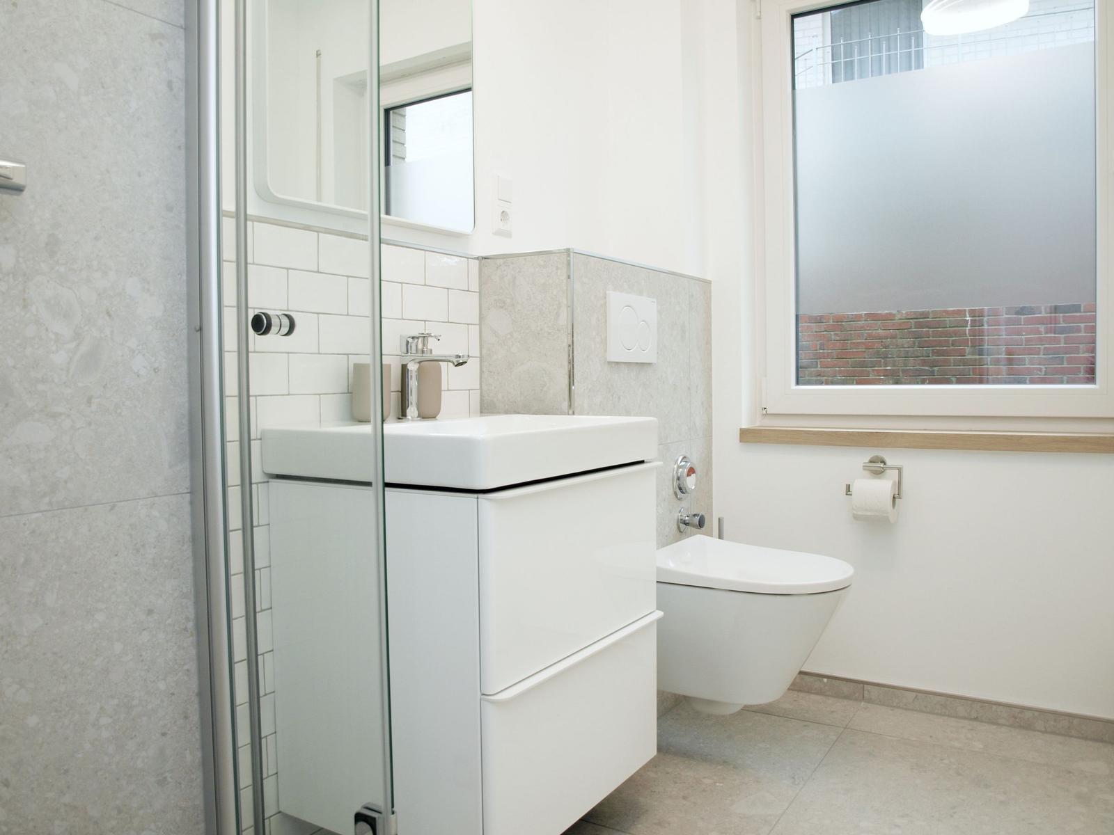 Bad mit Waschbecken, Toilette und Dusche. Fenster mit getöntem Glas.