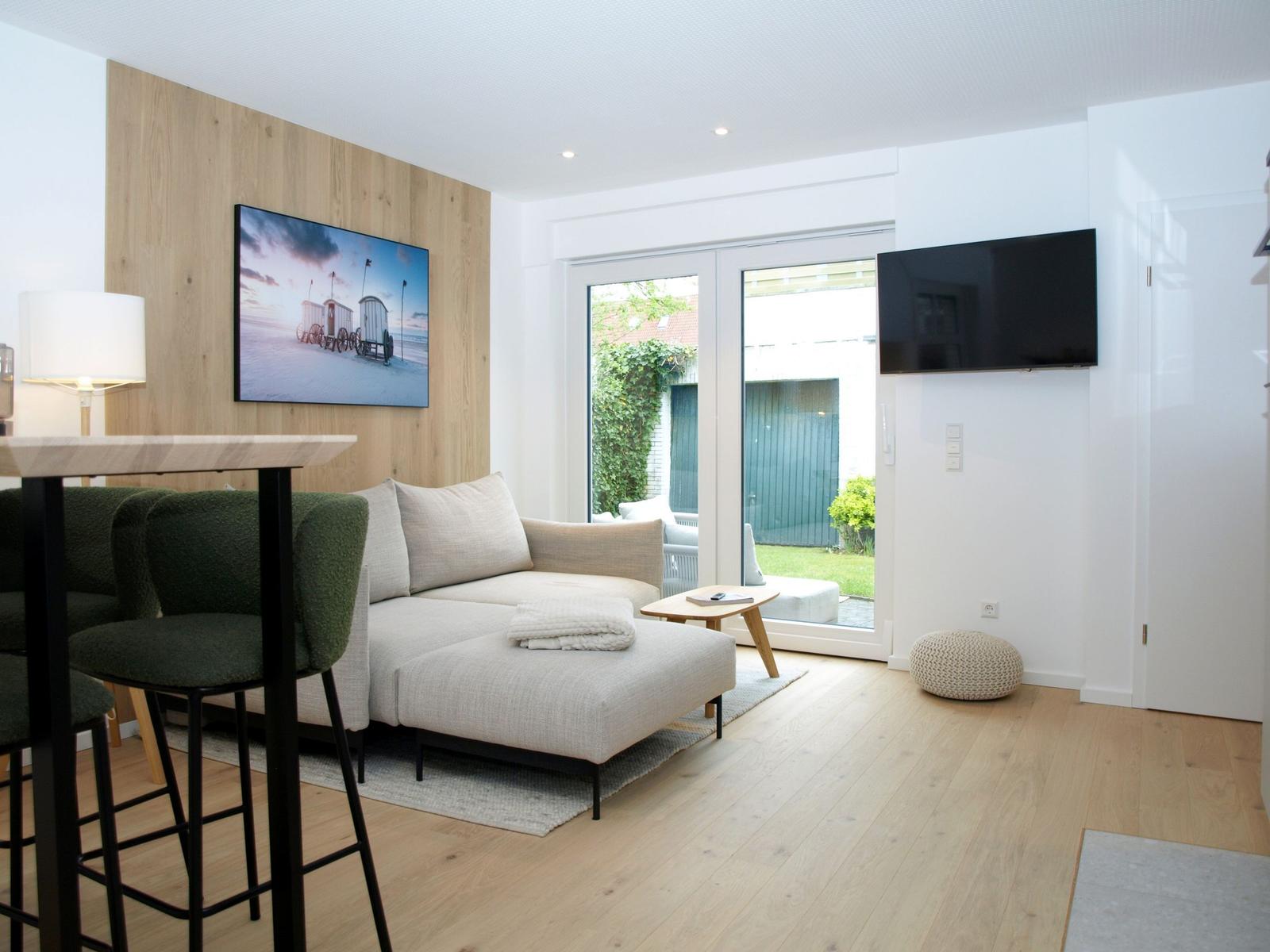Wohnbereich mit Sofa, Fernseher und Blick auf den Garten.
