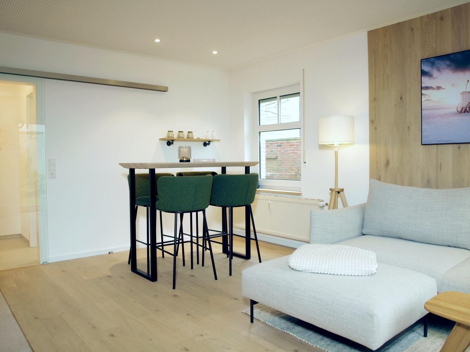 Wohnbereich mit Sofa, Esstisch und Fenster. Holzboden und Wandverkleidung.