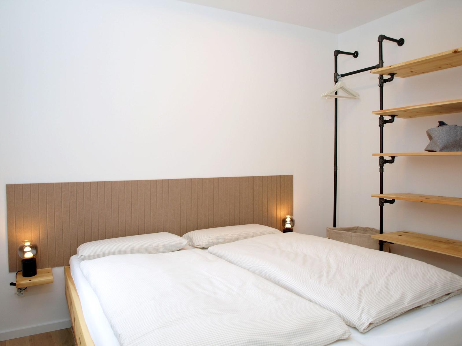 Schlafzimmer mit Doppelbett, Holzregal und Nachttischlampen.