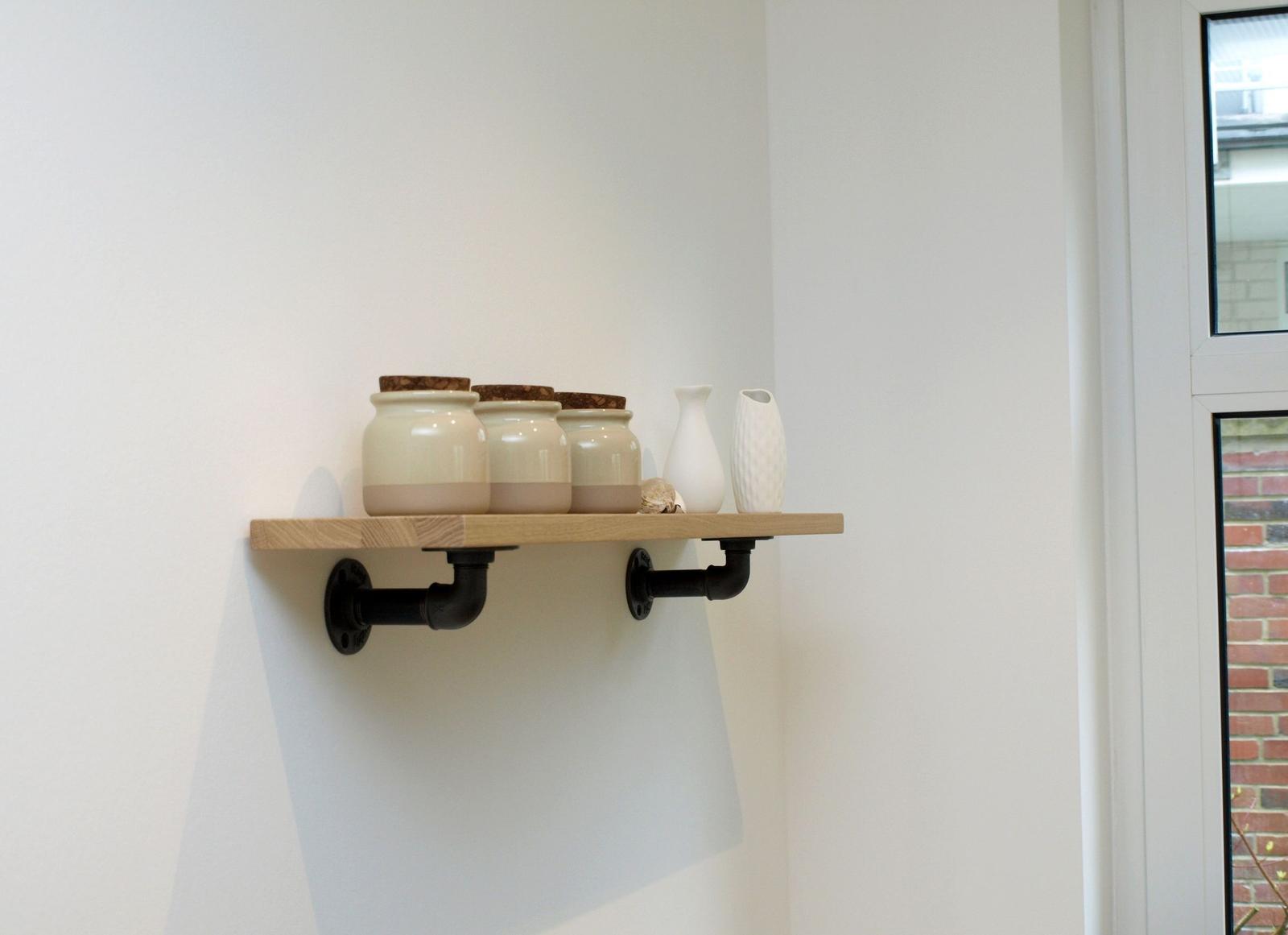 Holzregal mit drei Keramikdosen und zwei Vasen an der Wand.