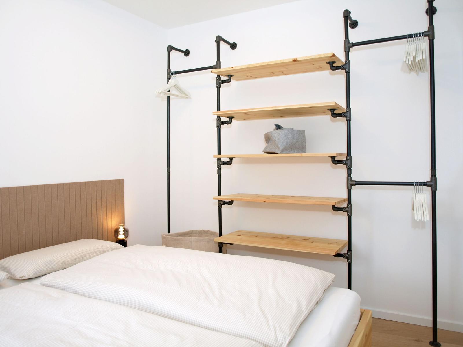 Schlafzimmer mit Bett, Kleidersystem und Nachttischlampe.