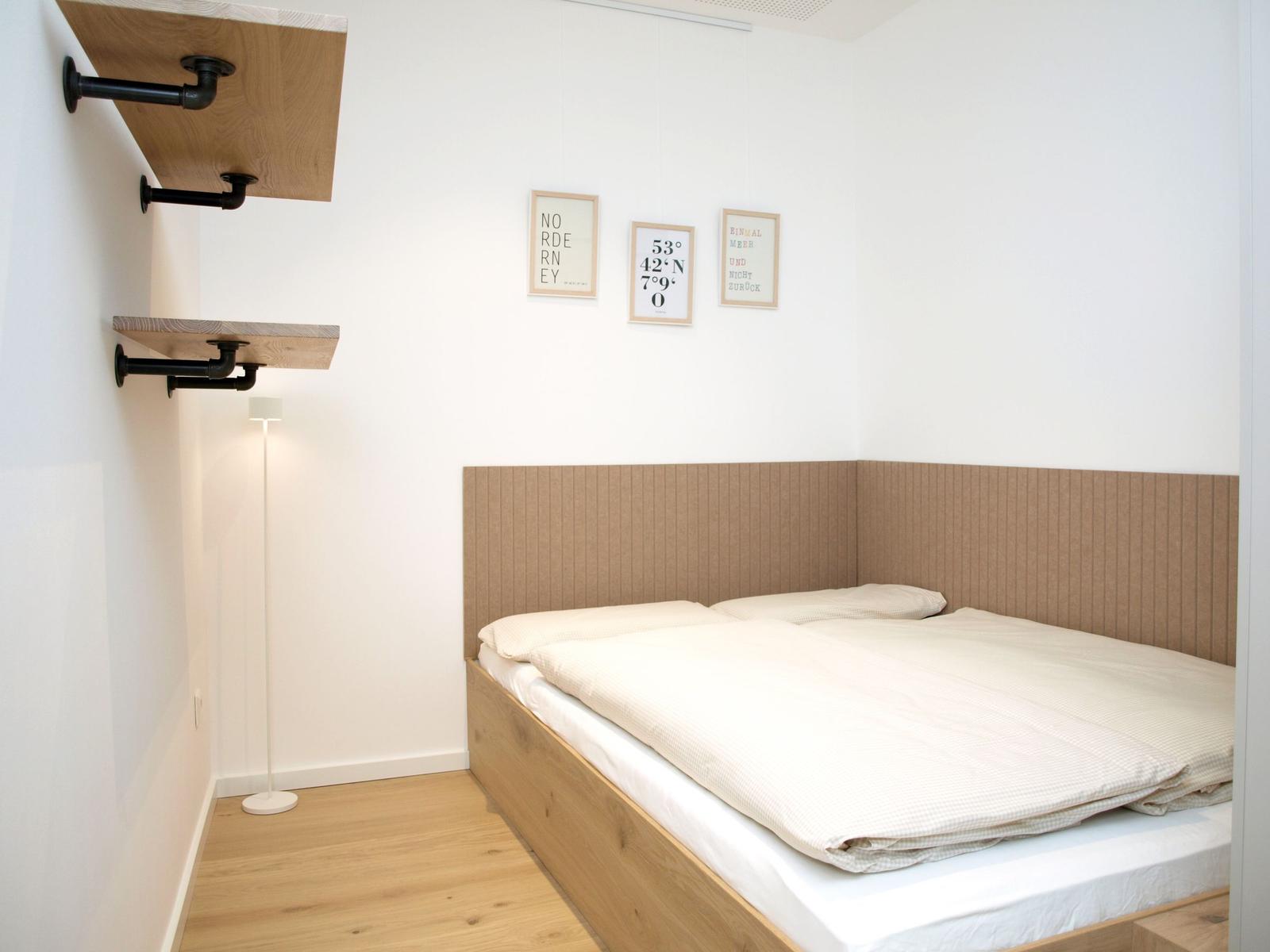 Ein Schlafzimmer mit Doppelbett, Holzboden und Wandregalen.