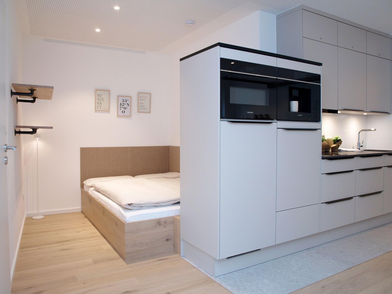 Schlafzimmer mit Bett und Küchenbereich mit integrierten Geräten.