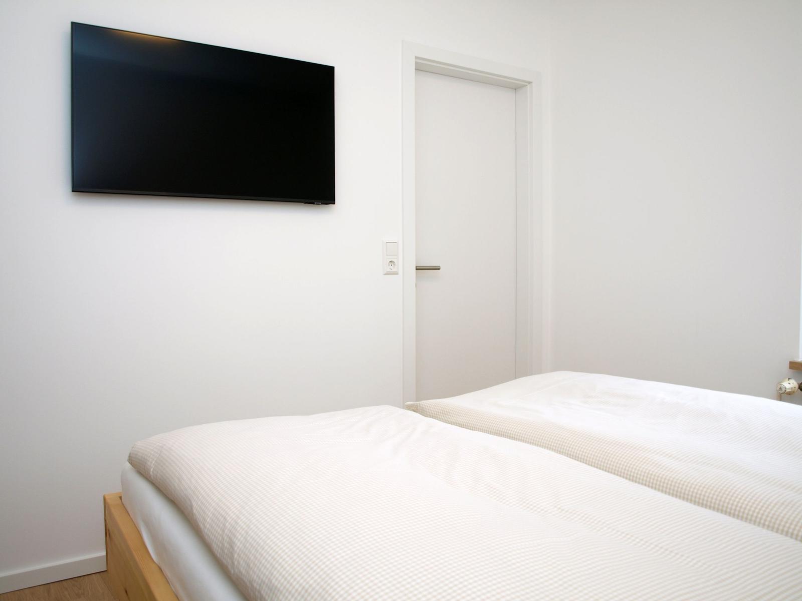 Schlafzimmer mit Bett, Wandfernseher und Tür.