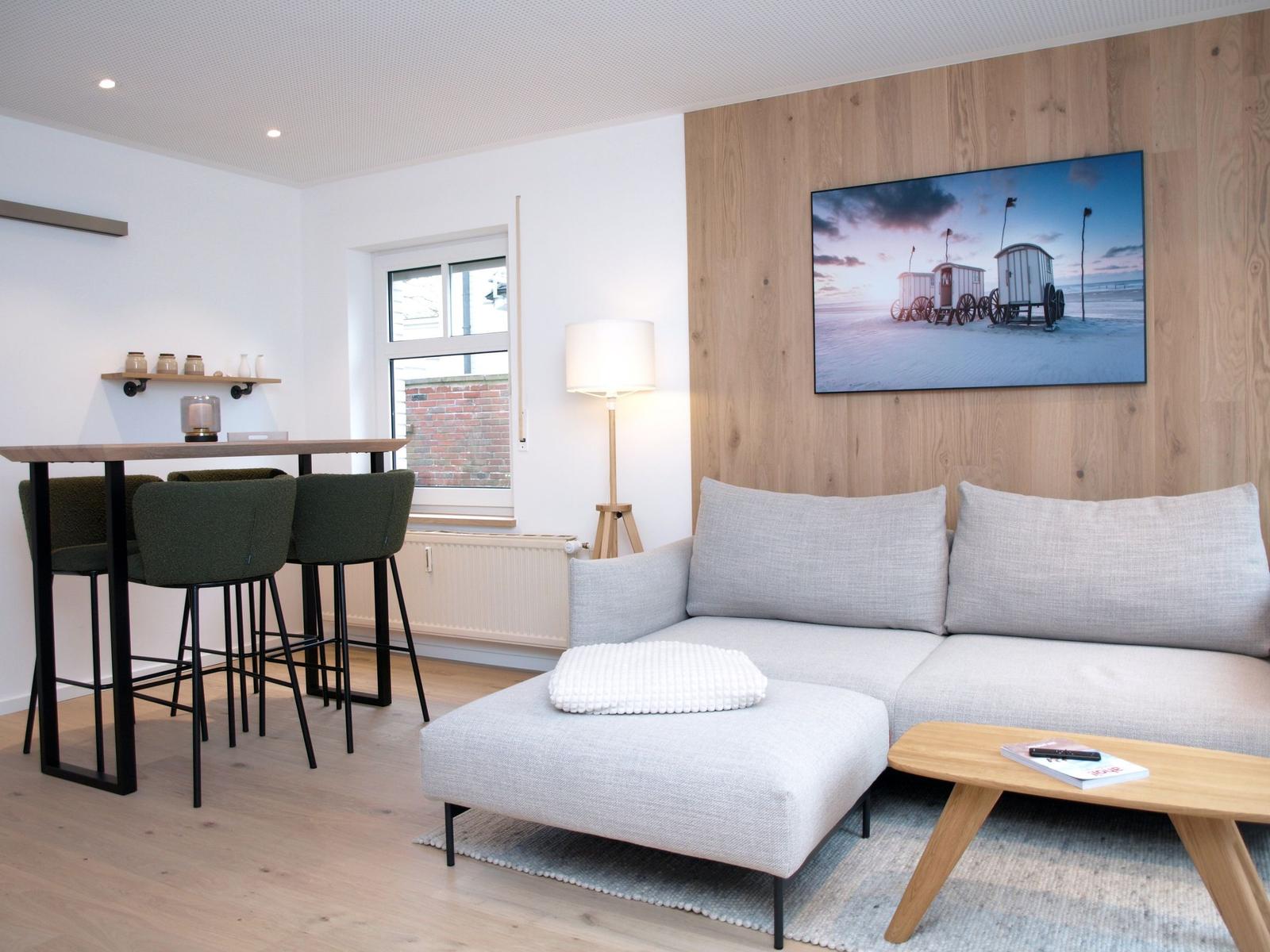 Wohnzimmer mit Sofa, Couchtisch und Barhocker. Wandbild zeigt Strandkörbe.