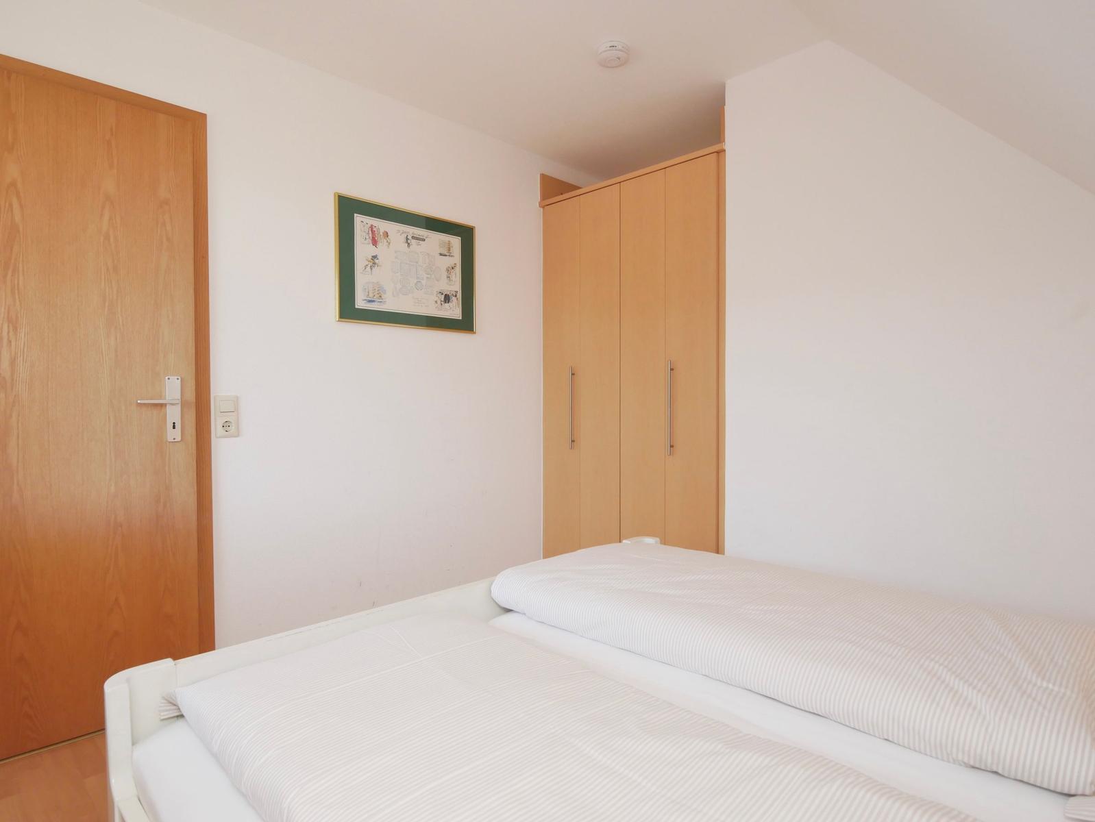Schlafzimmer mit Bett, Kleiderschrank und Tür. Wandbild über dem Bett.