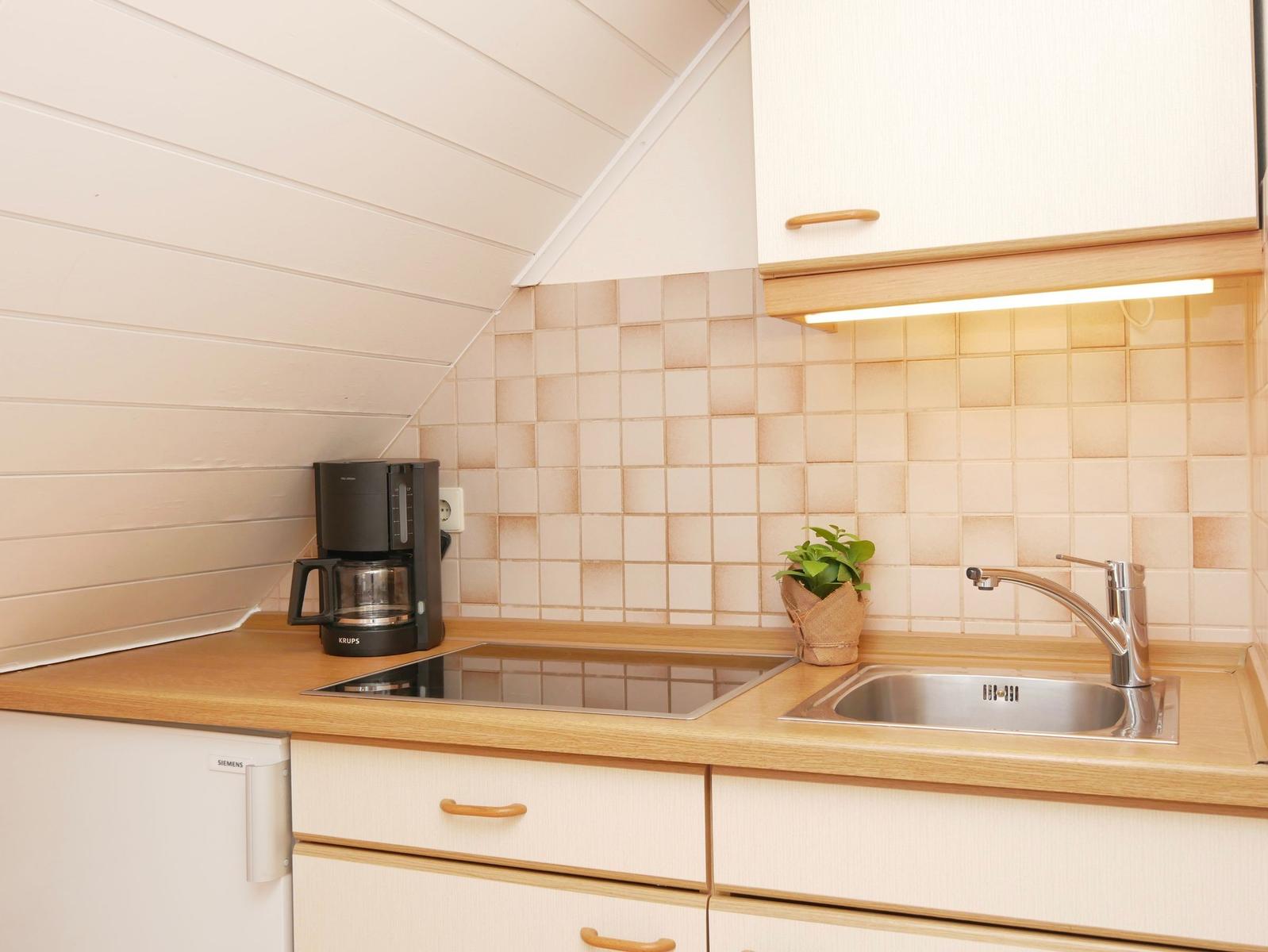 Küche mit Kaffeemaschine, Spüle und Kühlschrank unter schrägem Dach.