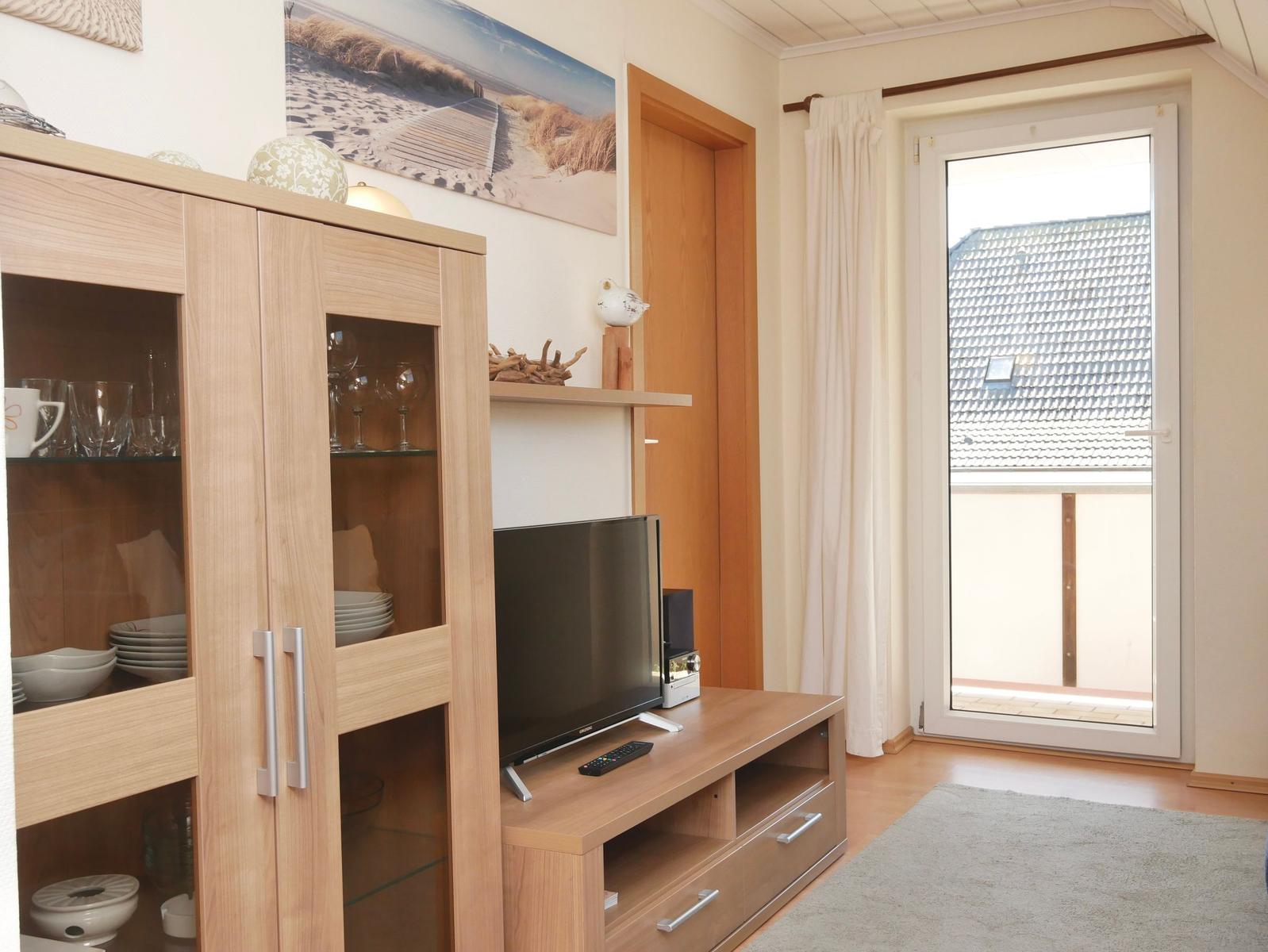 Wohnzimmer mit Holzmöbeln, Fernseher und Blick auf Balkon