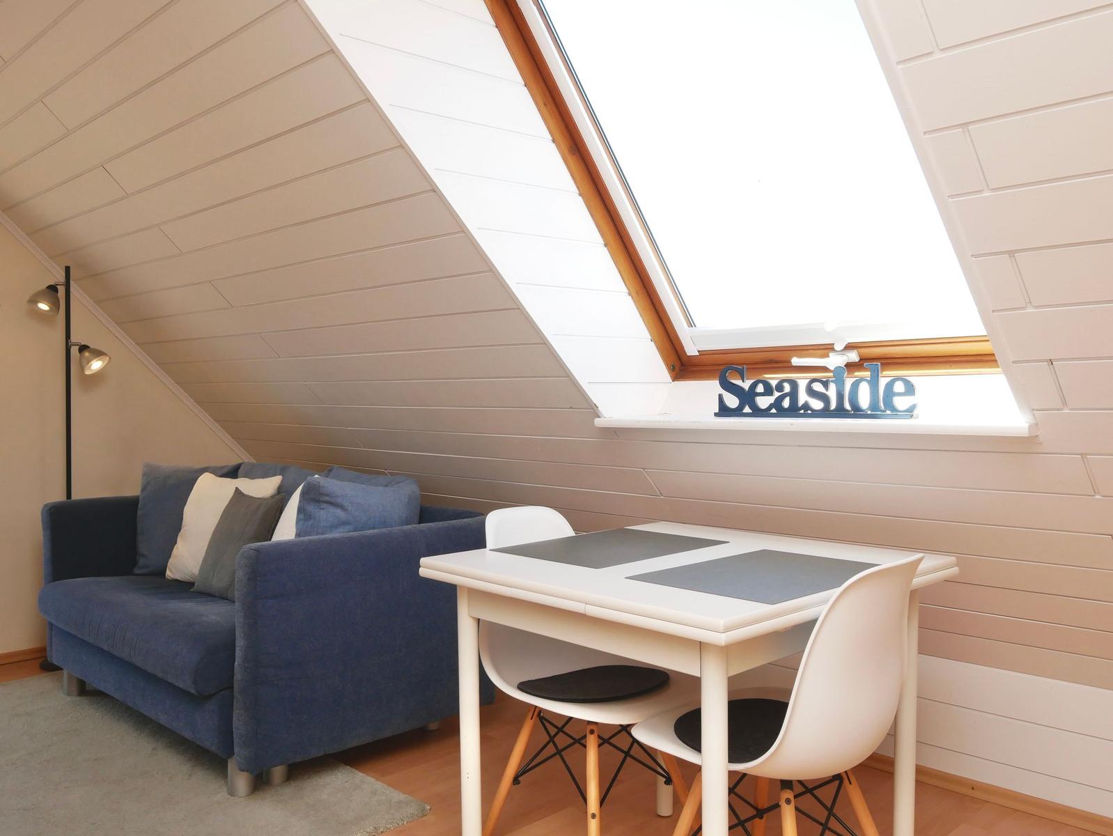 Schlafzimmer mit Sofa, Tisch und Stühlen unter Dachschrägen mit Dachfenster.