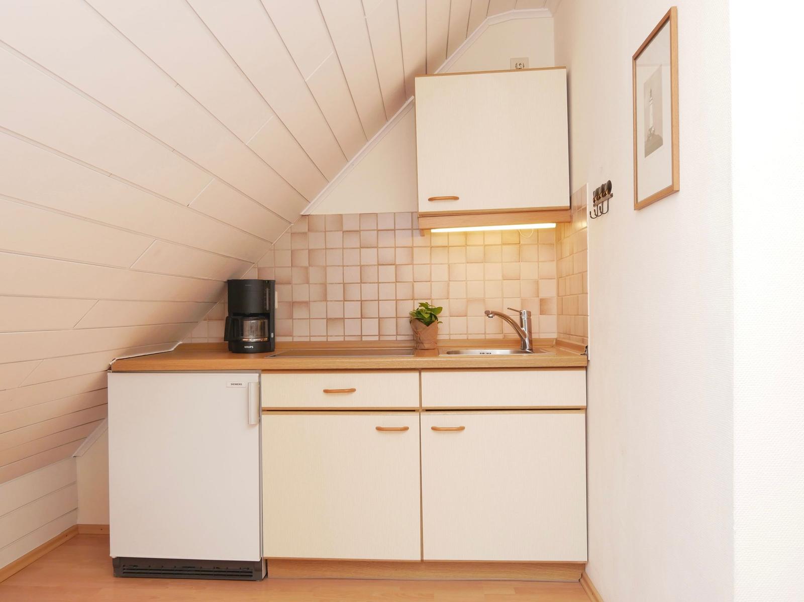 Küche mit Arbeitsplatte, Spüle, Kühlschrank und Kaffeemaschine unter schrägem Dach.