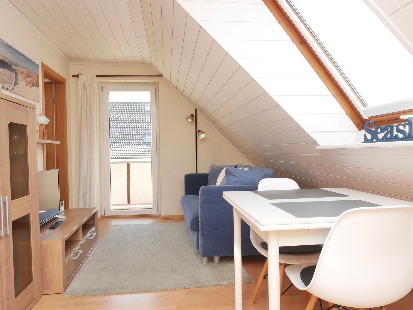 Wohn- und Essbereich mit Sofa, Tisch, Stühlen und Dachfenster. Tür führt auf Balkon.
