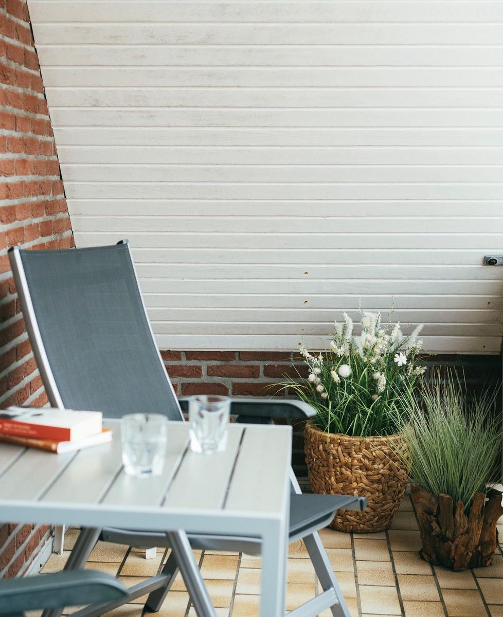Terrasse mit Stuhl, Tisch, Gläsern und Pflanzen vor weißer Holzwand und Backsteinmauer.