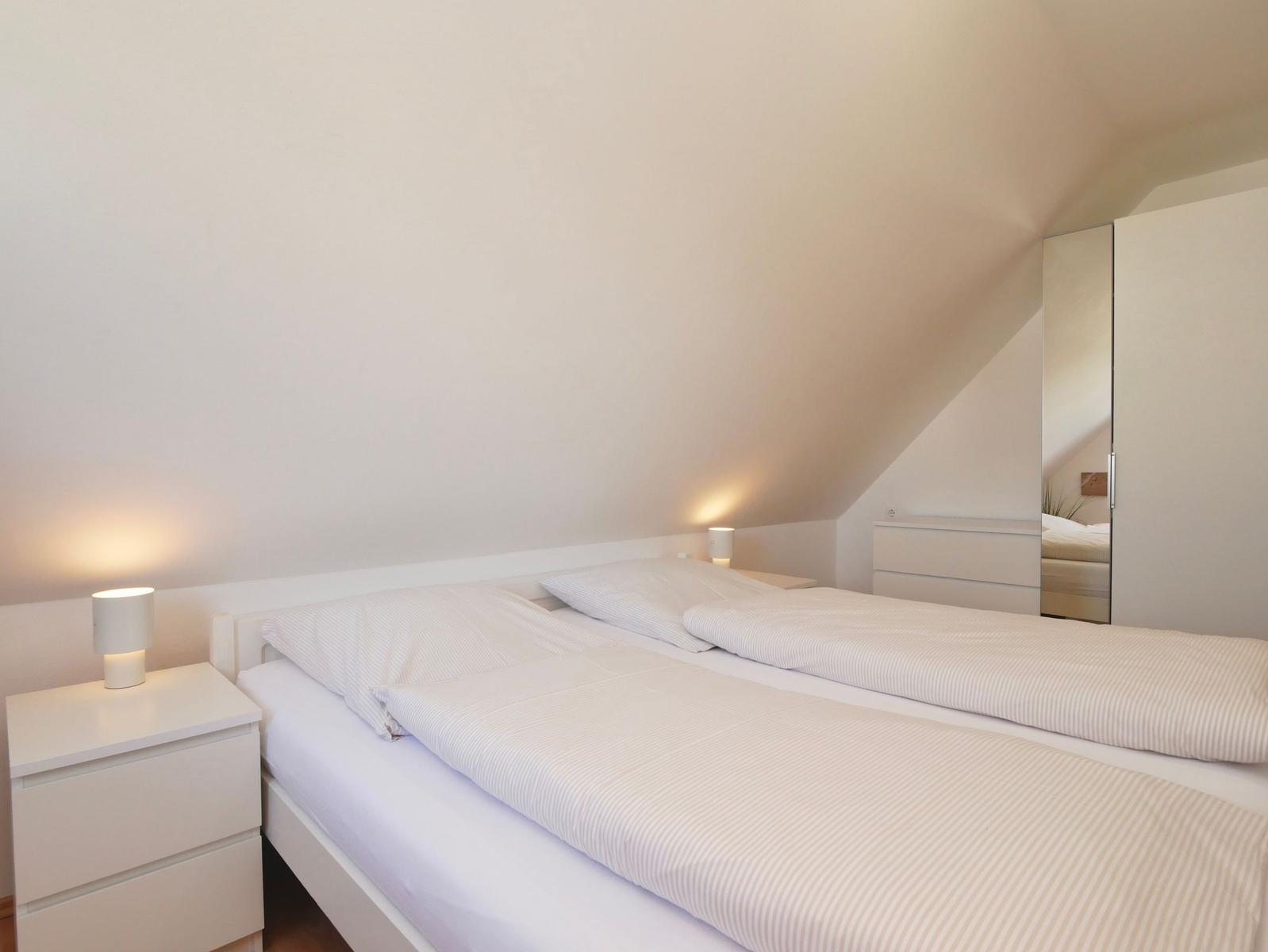 Schlafzimmer mit Doppelbett, Nachttisch und Spiegelschrank unter schrägem Dach.
