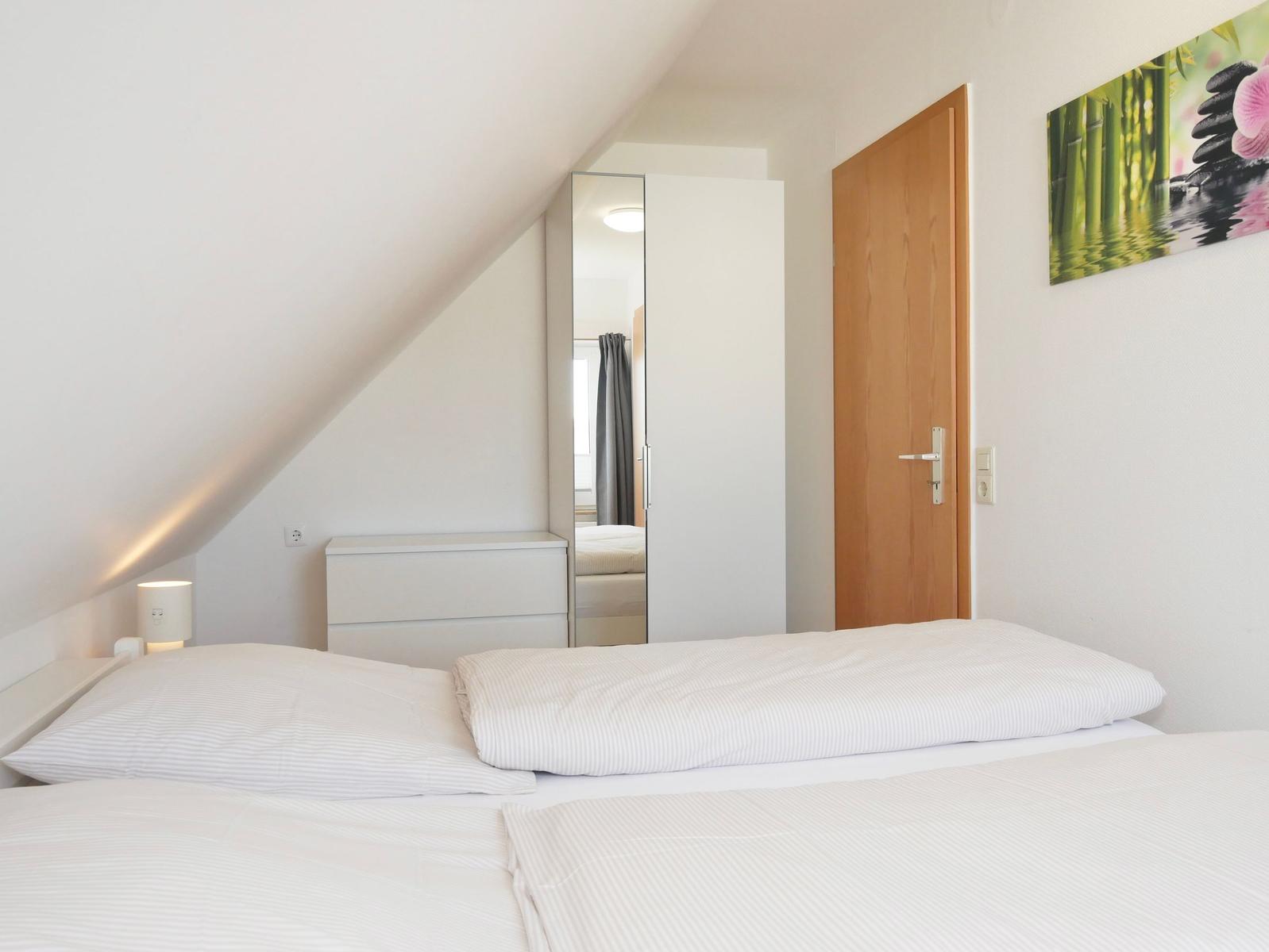 Schlafzimmer mit Dachschräge, Bett, Schrank und Wandbild.