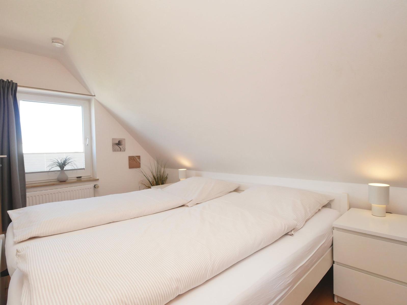 Schlafzimmer mit Doppelbett, Nachttisch und Fenster unter Dachschräge.