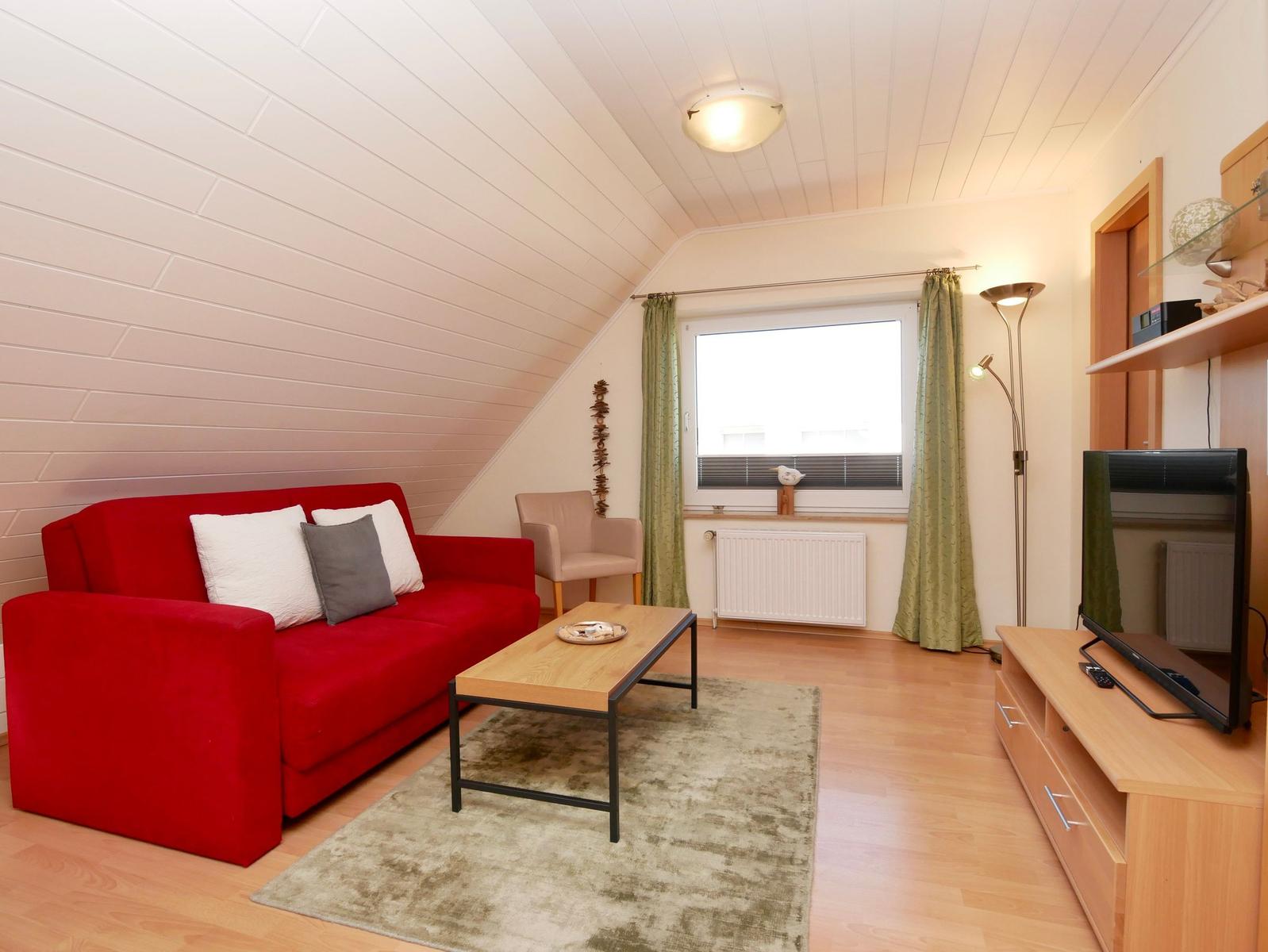 Ein Wohnzimmer mit rotem Sofa, Holztisch und Fernseher.