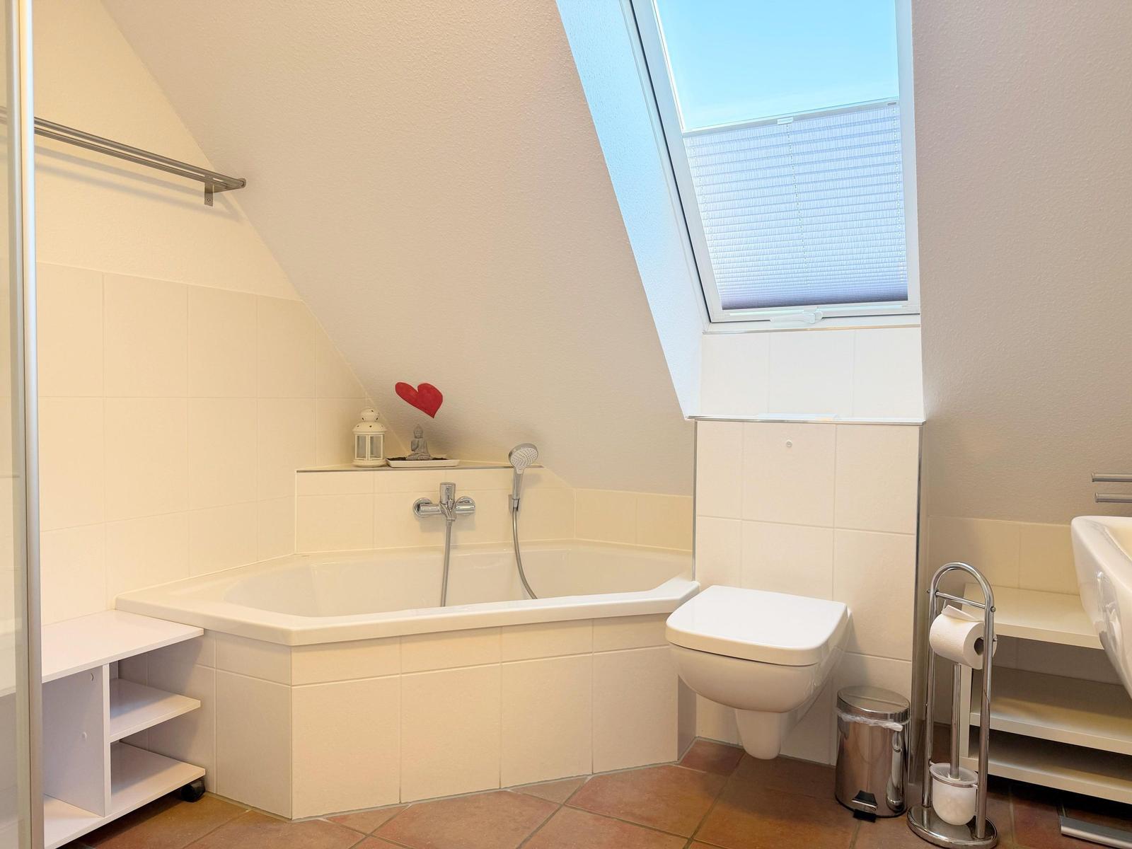 Badezimmer mit Badewanne, Toilette und Duschbereich unter Dachschrägen.
