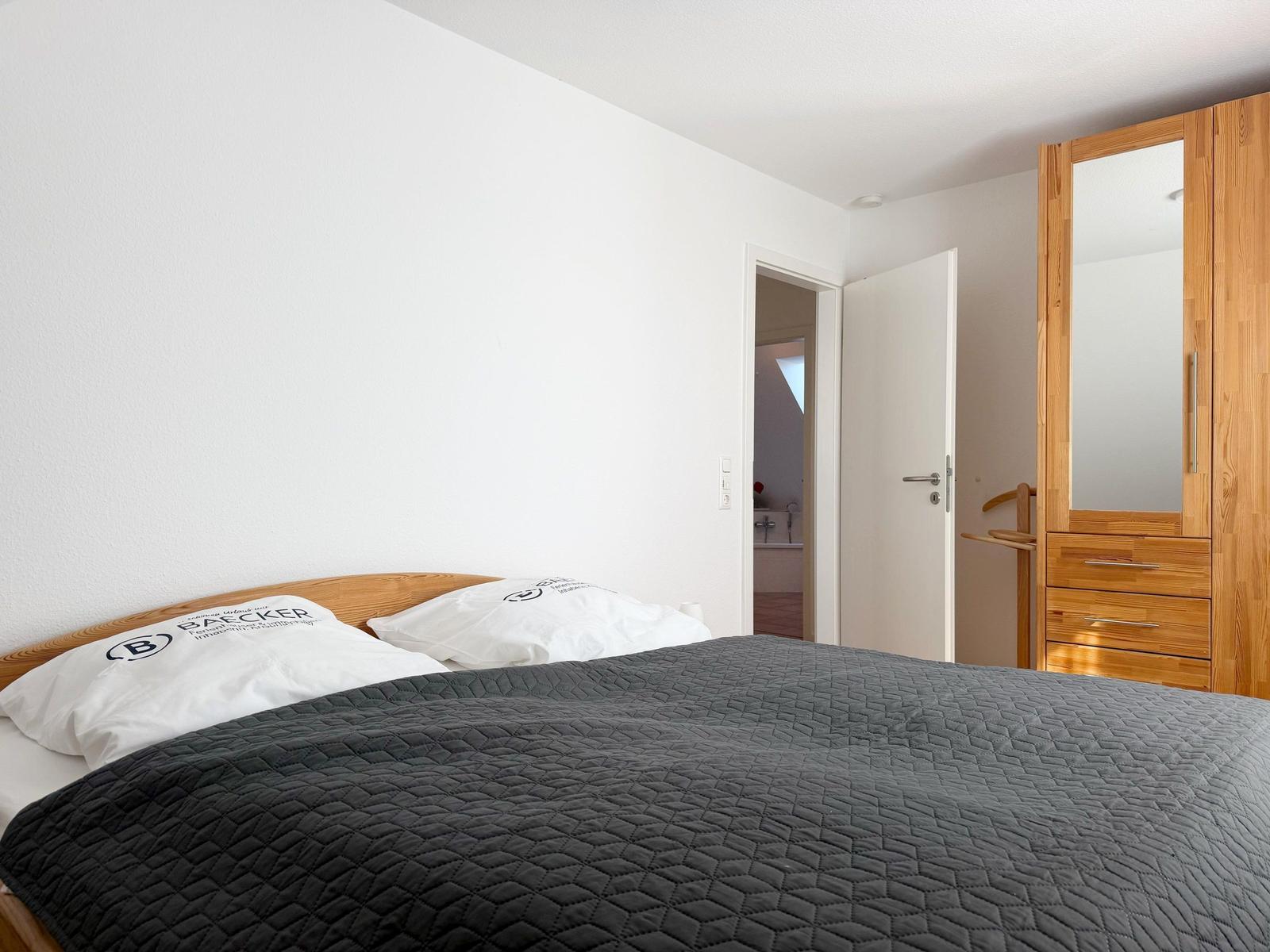 Schlafzimmer mit Bett, Kleiderschrank und Tür zum Bad.