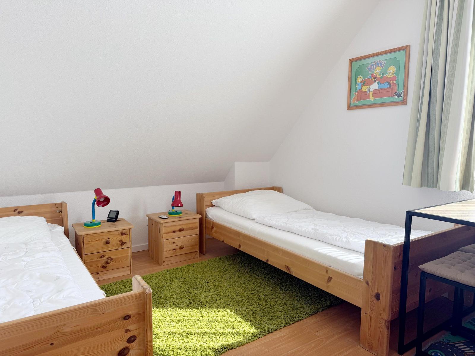 Zwei Einzelbetten, Nachttische mit Lampen, grüner Teppich, Wandbild und Fenster mit Vorhängen.