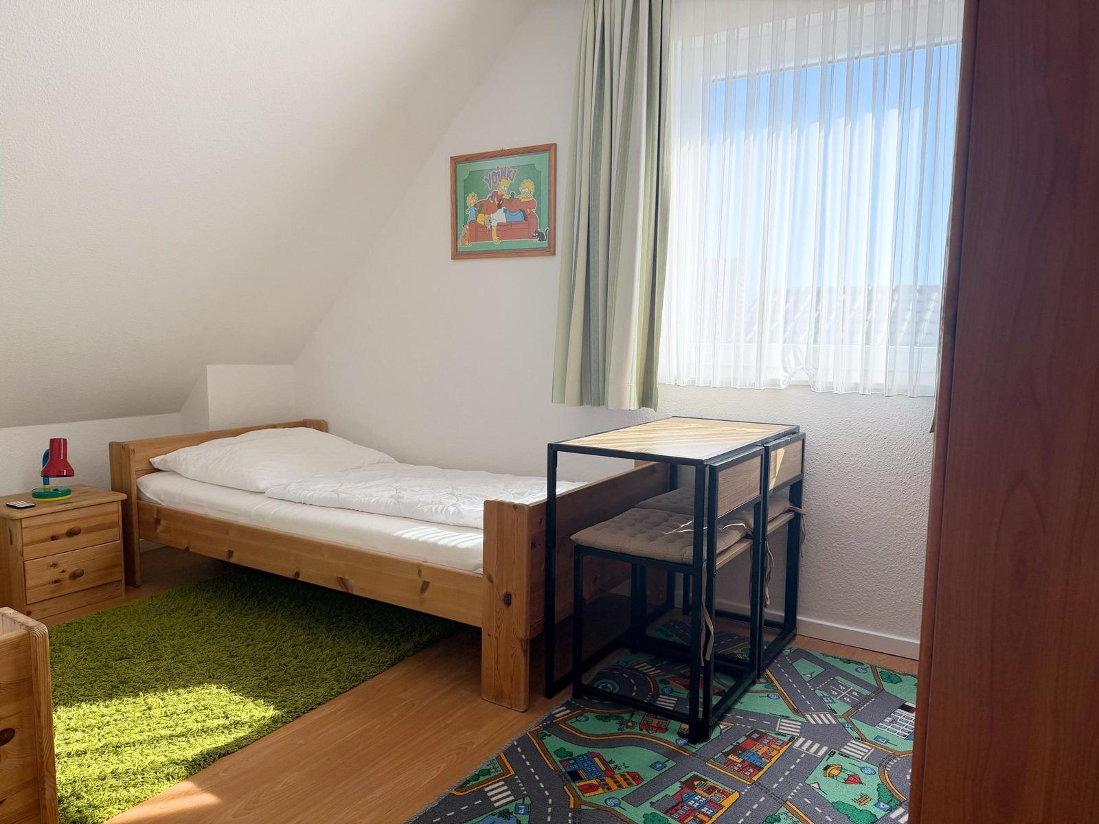 Ein Schlafzimmer mit einem Bett, einem Schreibtisch und einem Fenster mit Vorhängen.
