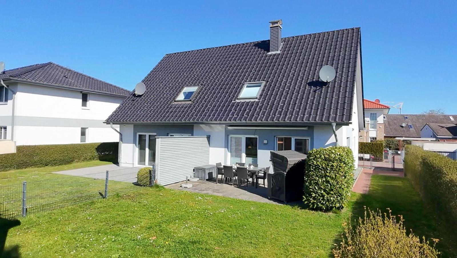 Modernes Haus mit Garten, Terrasse und Grill. Dach mit Dachfenstern und Satellitenschüsseln.