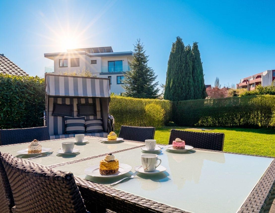 Terrasse mit Esstisch, Sonnenliege und Kuchen unter blauem Himmel.