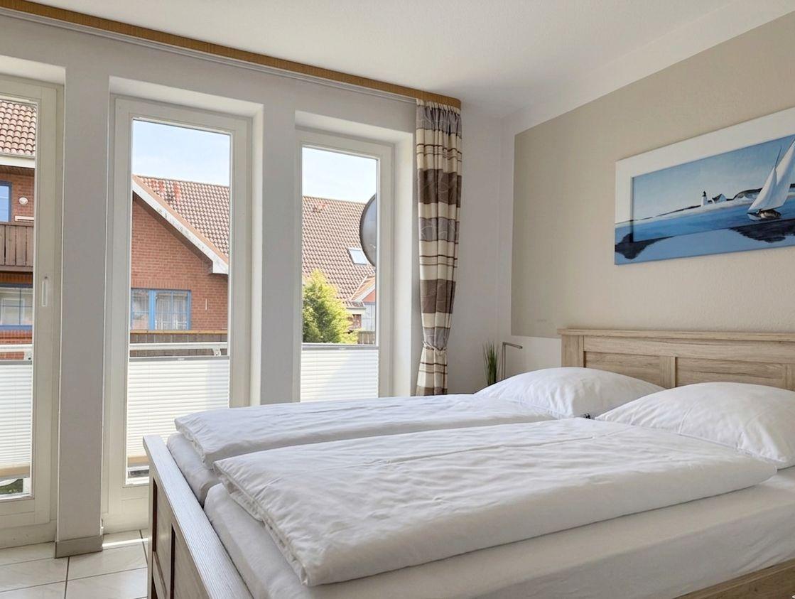Schlafzimmer mit Doppelbett, Fenster zur Terrasse und Wandbild mit Segelboot.