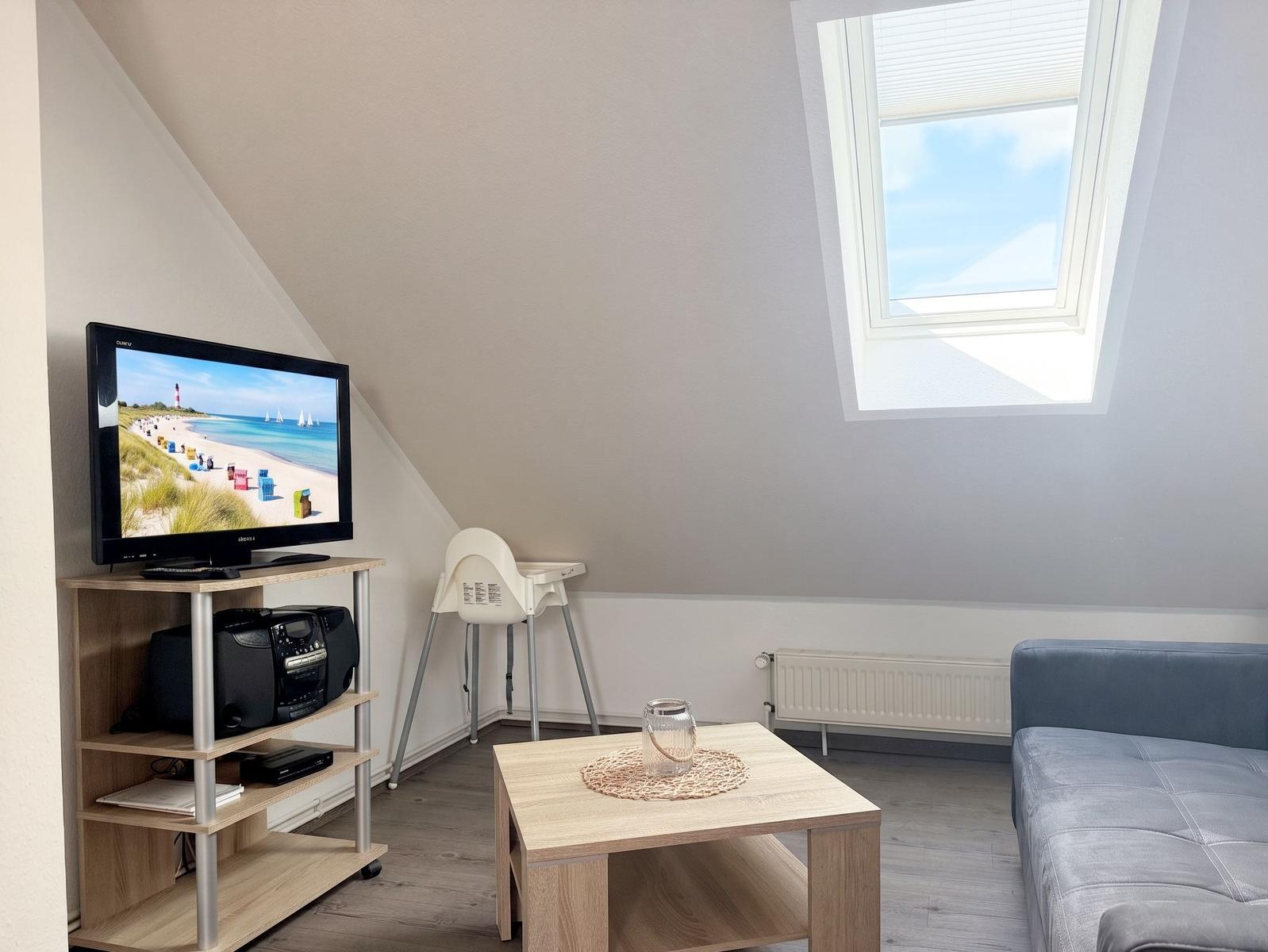 Wohnzimmer mit TV, Sitzgarnitur, Kindersitz und Dachfenster.