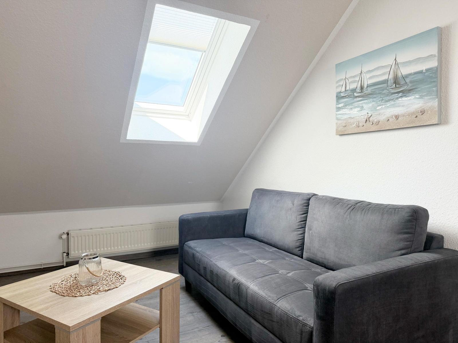 Dachgeschosswohnung mit Sofa, Tisch und Dachfenster. Wandbild mit Segelbooten.