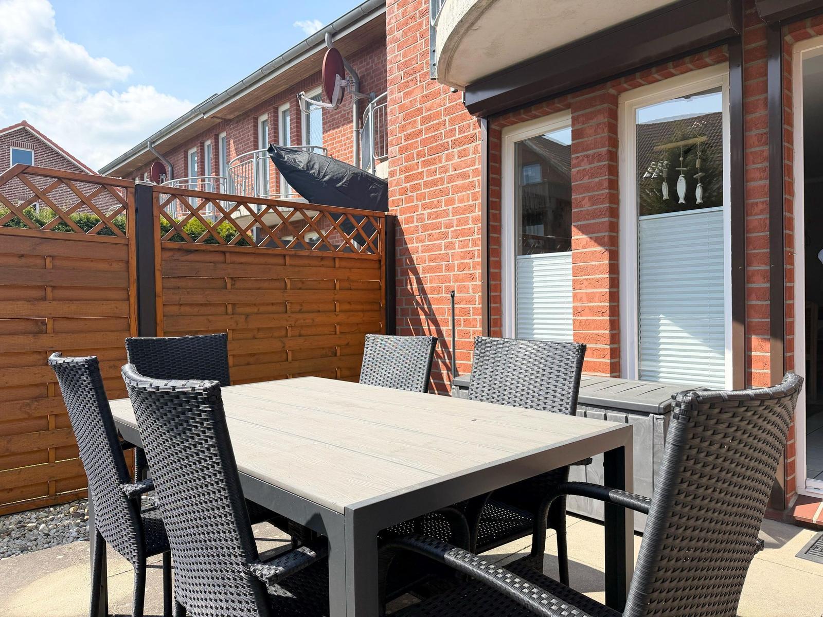 Terrasse mit Tisch und sechs Stühlen vor rotem Backsteinhaus.