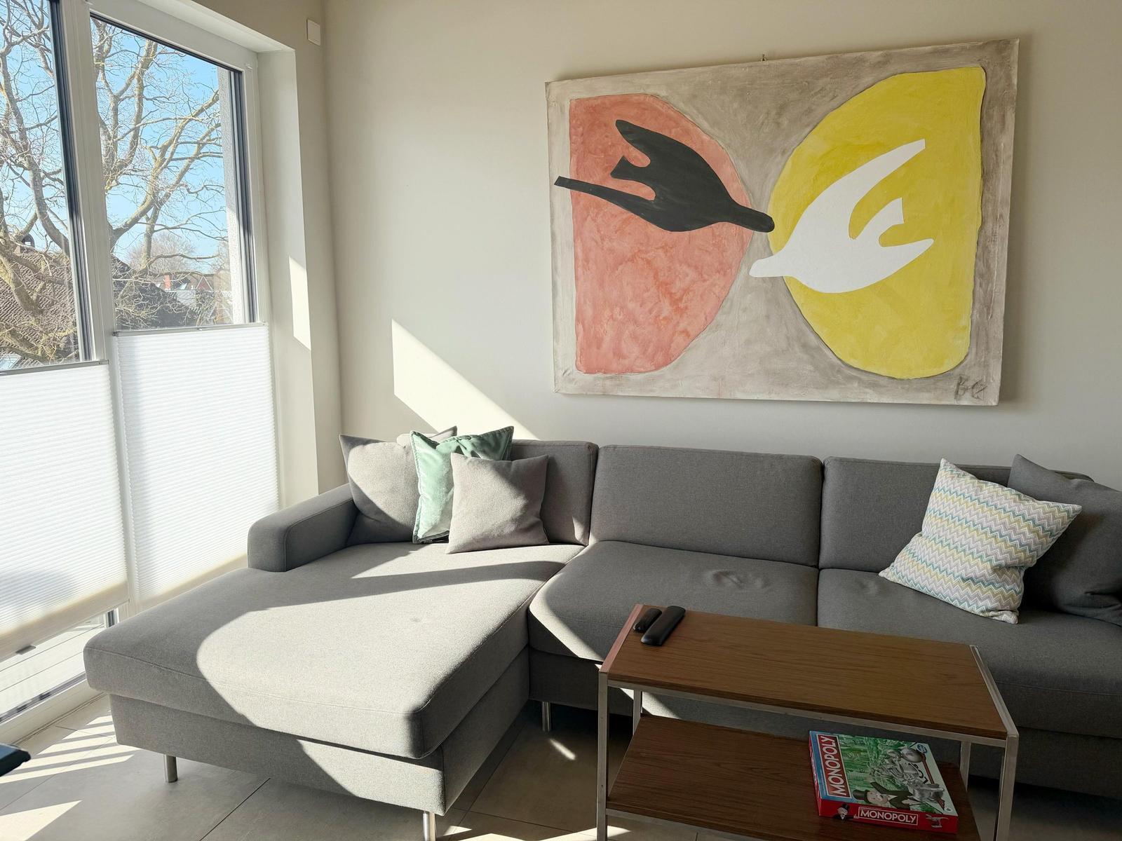 Ein grauer Sofa mit Kissen und einem Holztisch vor einer Wand mit Kunstwerk.